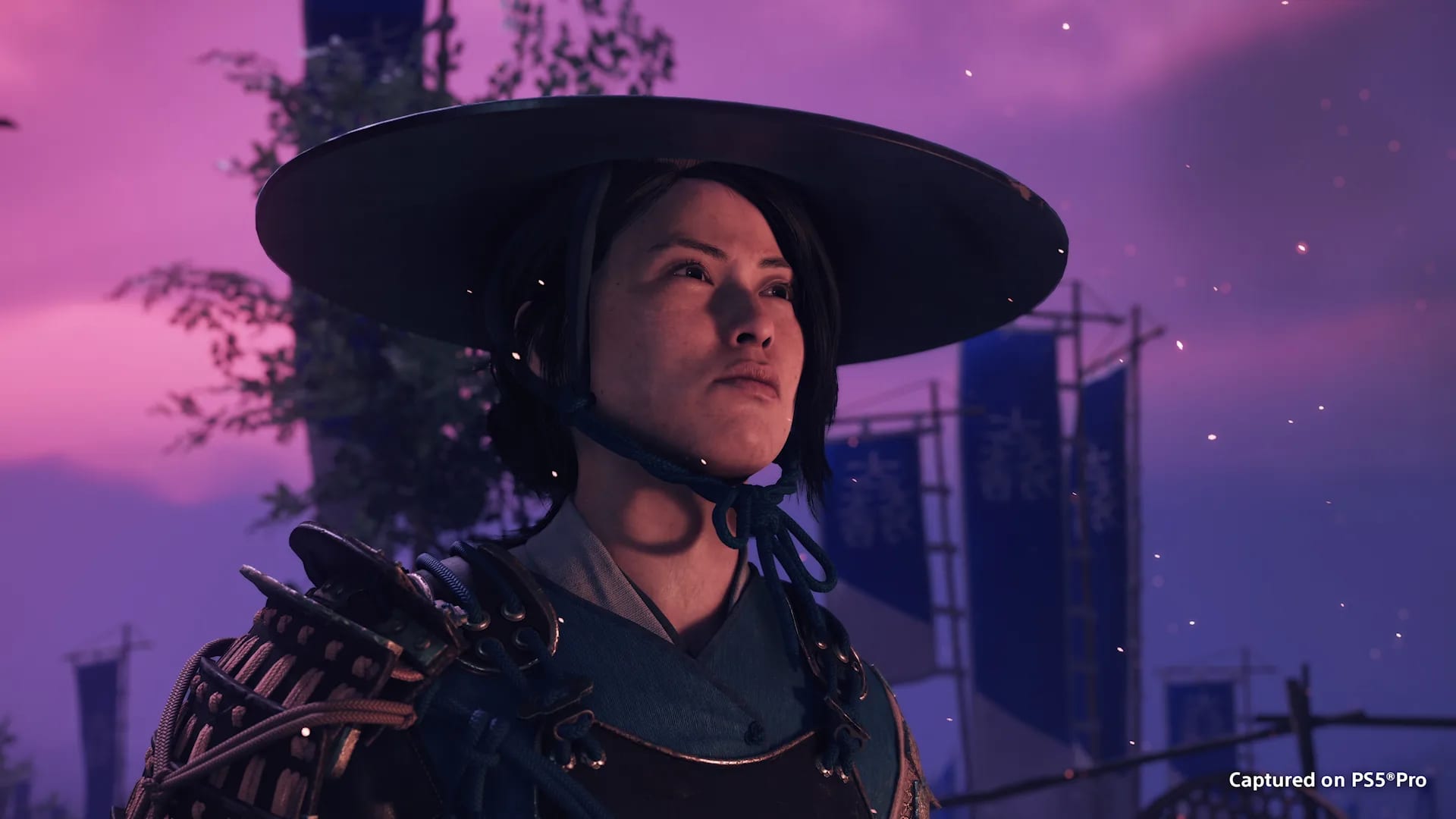 Primer plano de una guerrera con sombrero de ala ancha y armadura, mirando hacia arriba bajo un cielo violeta, con estandartes azules al fondo.