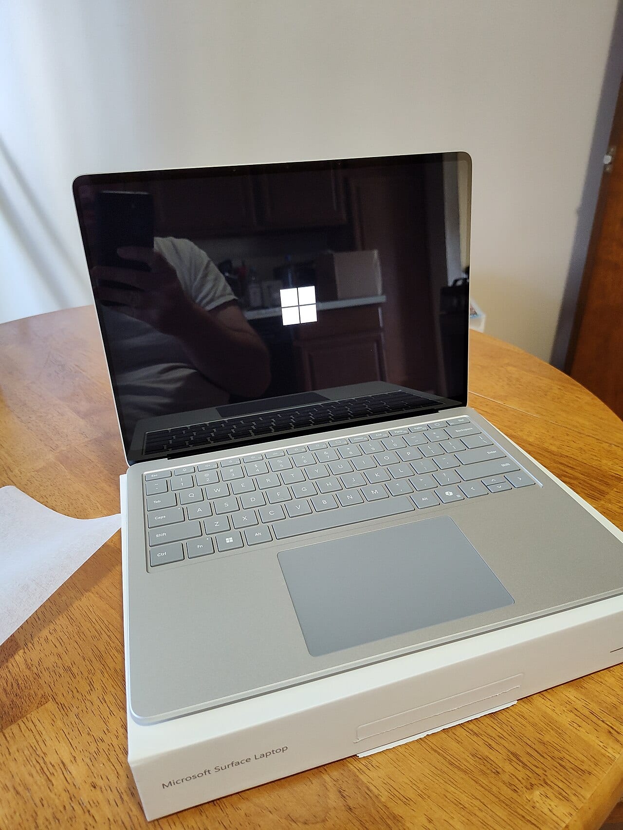 Laptop Microsoft Surface abierta sobre su caja, con el logotipo de Windows en la pantalla durante el arranque, en una mesa de madera.