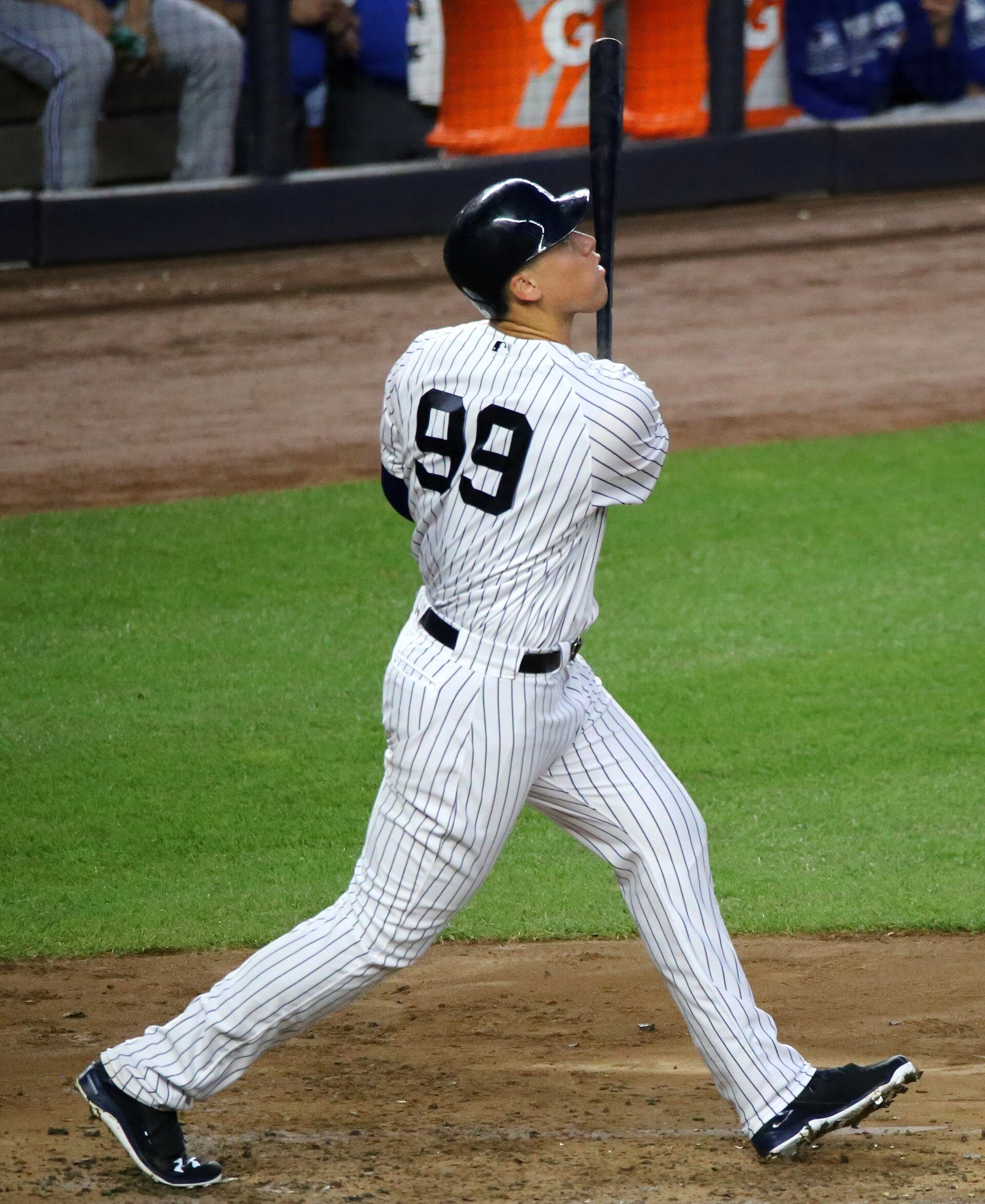 A batter in white pinstripes and number 99 watches the ball after his swing, bat held high.