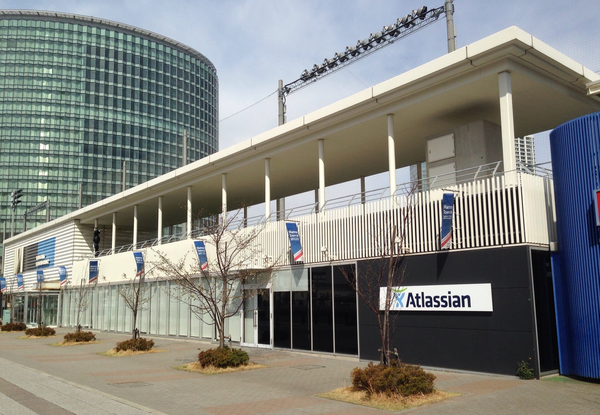Two-story office building with a white Atlassian sign on a black wall and a glass tower behind it.