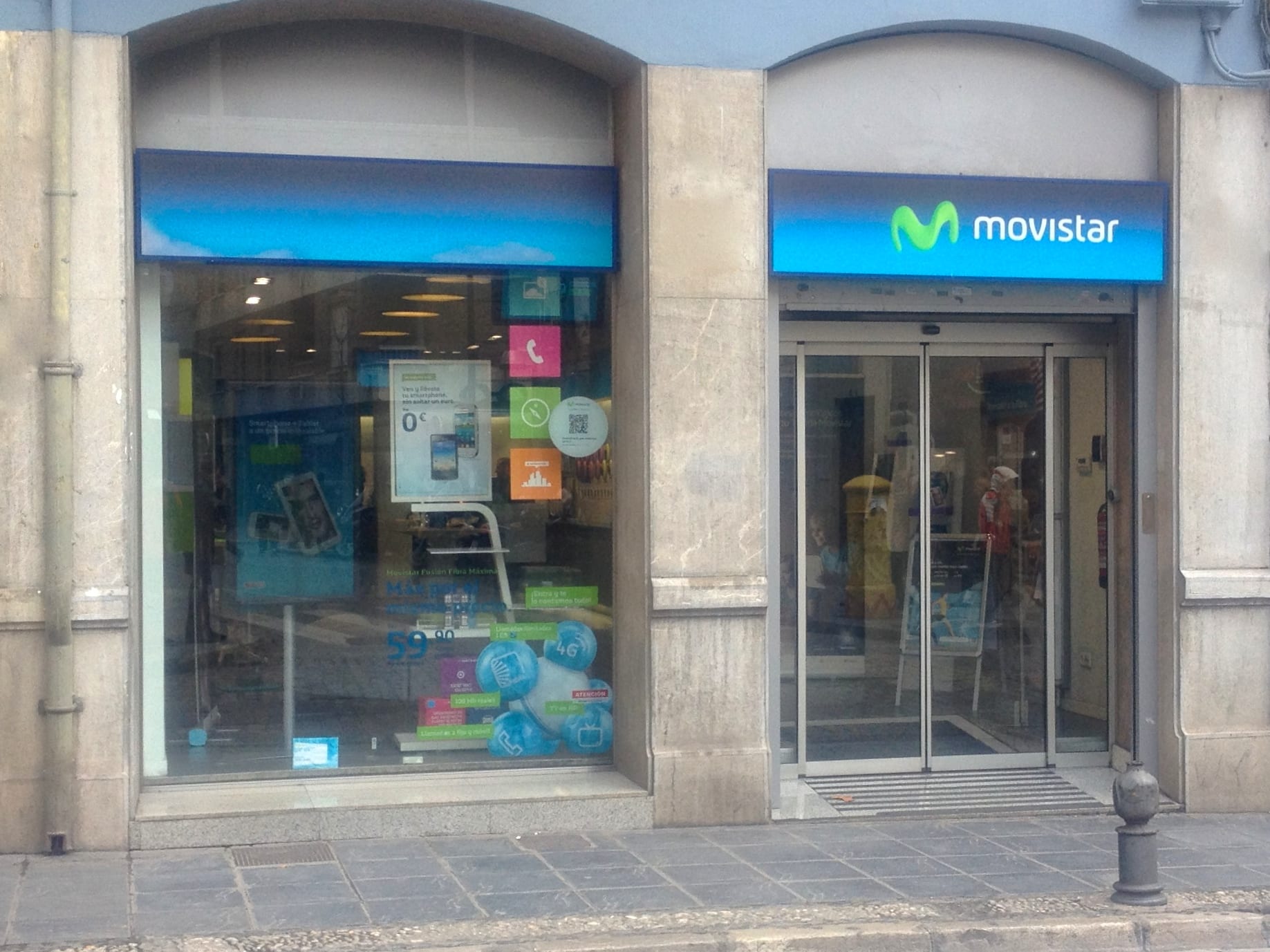 Front of a Movistar store with a blue sign and a window covered in promotional posters.