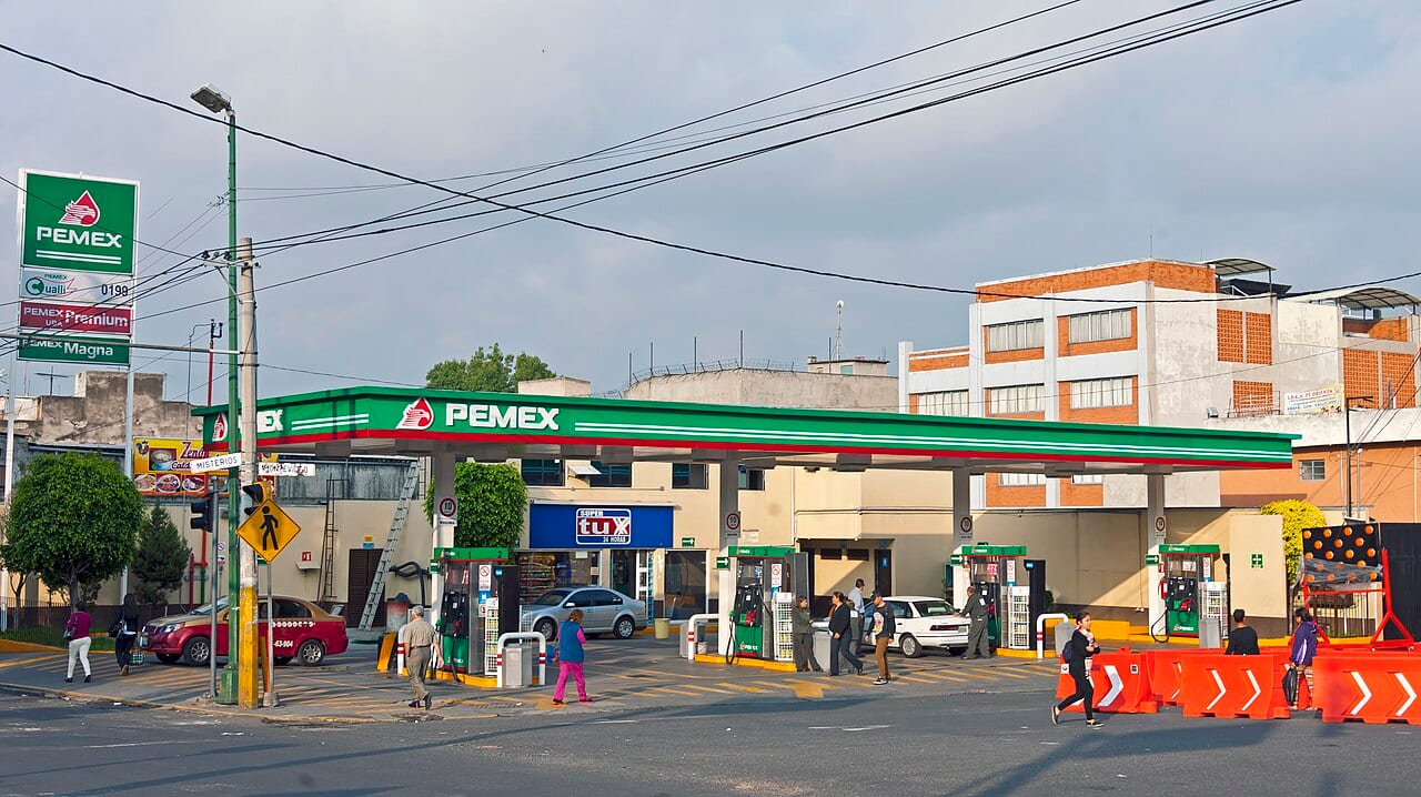 Gasolinera Pemex de día, con las etiquetas de Magna y Premium en el tótem y clientes cargando combustible.