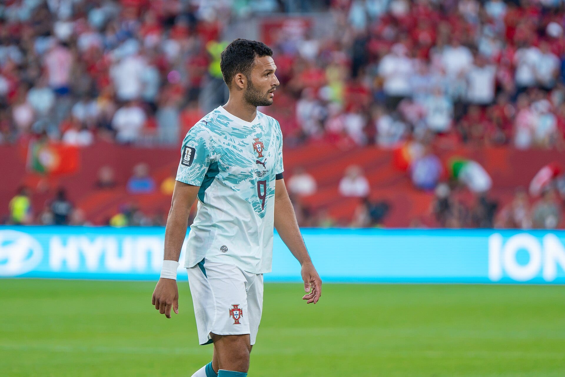 Gonçalo Ramos, in Portugal's white and turquoise number 9 shirt, walks across the pitch with a blurred crowd behind him.