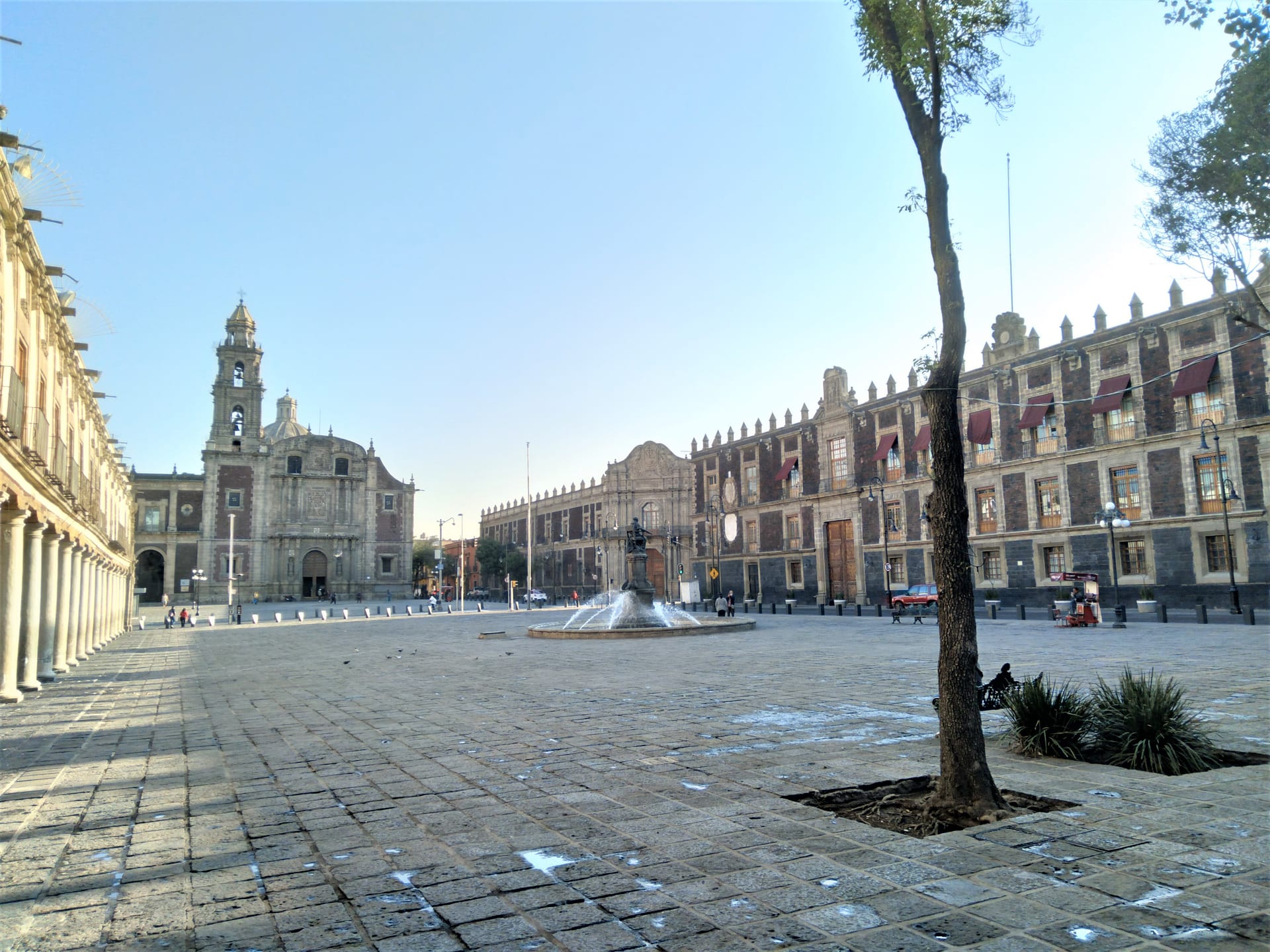Plaza de Santo Domingo con piso de adoquín y una fuente al centro; a la izquierda, la iglesia, y a la derecha, un edificio colonial de tezontle.