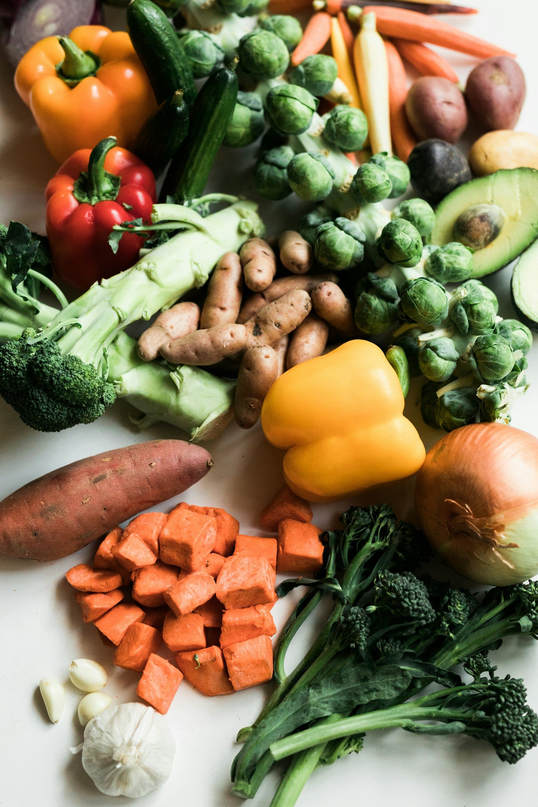 Verduras frescas como brócoli, pimientos y coles de Bruselas sobre una superficie blanca.