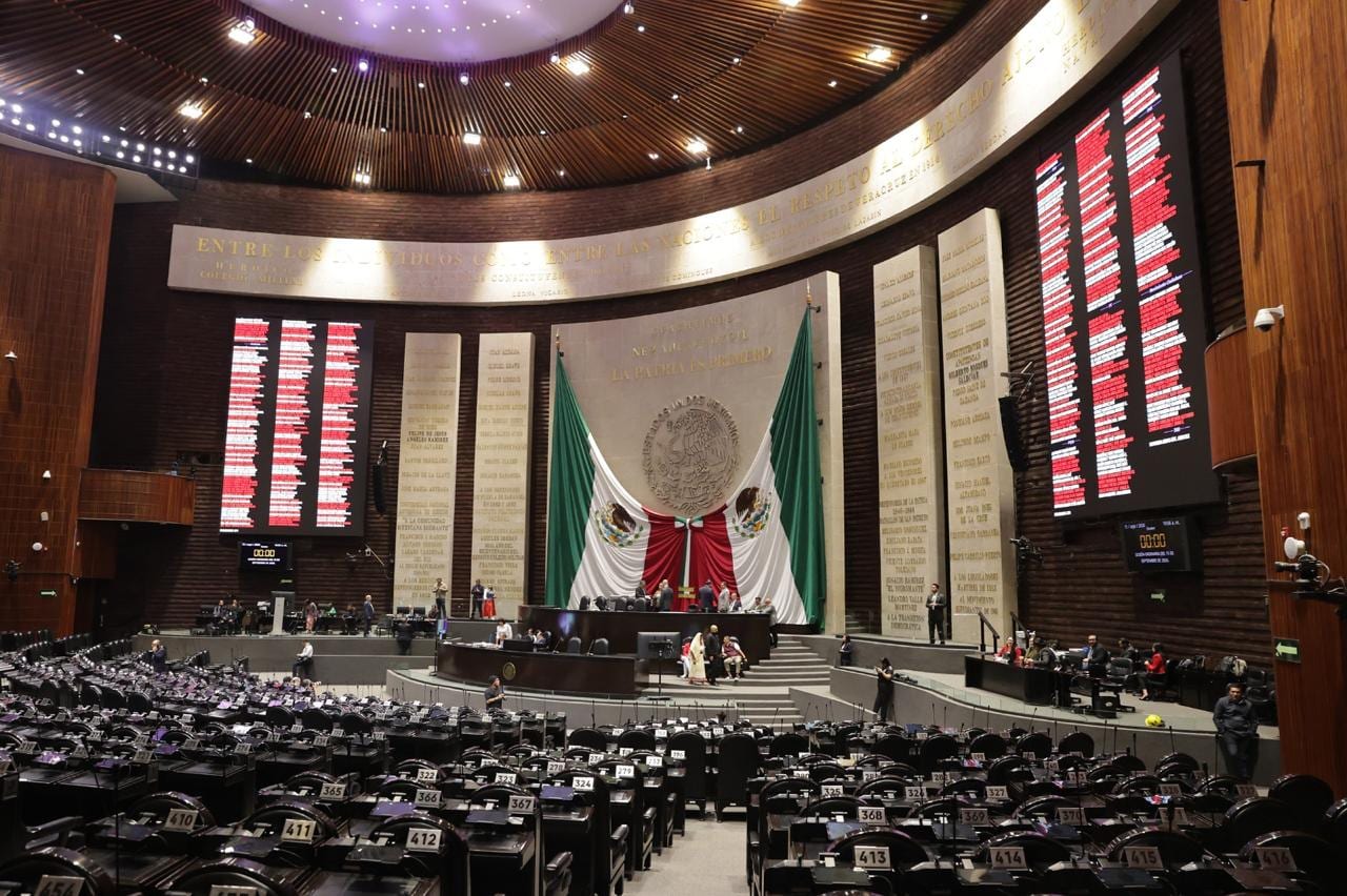 Salón de sesiones de la Cámara de Diputados con las curules vacías, las pantallas de votación a los lados y la bandera de México al fondo.