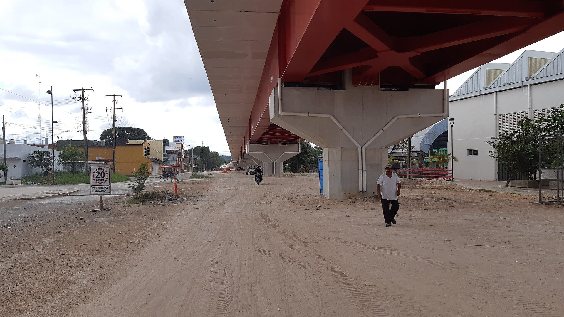 Un viaducto elevado de estructura roja y soportes de concreto sobre una calle de tierra en Escárcega, Campeche.