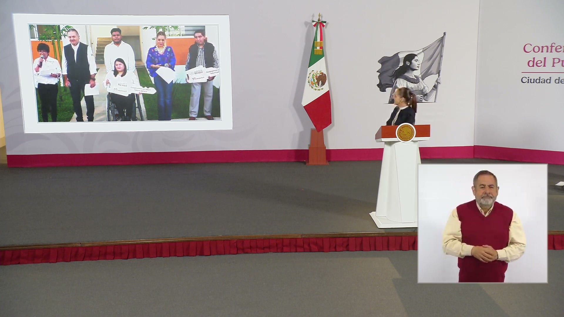 La presidenta Claudia Sheinbaum junto a su podio, con una pantalla que muestra la entrega de llaves de viviendas.