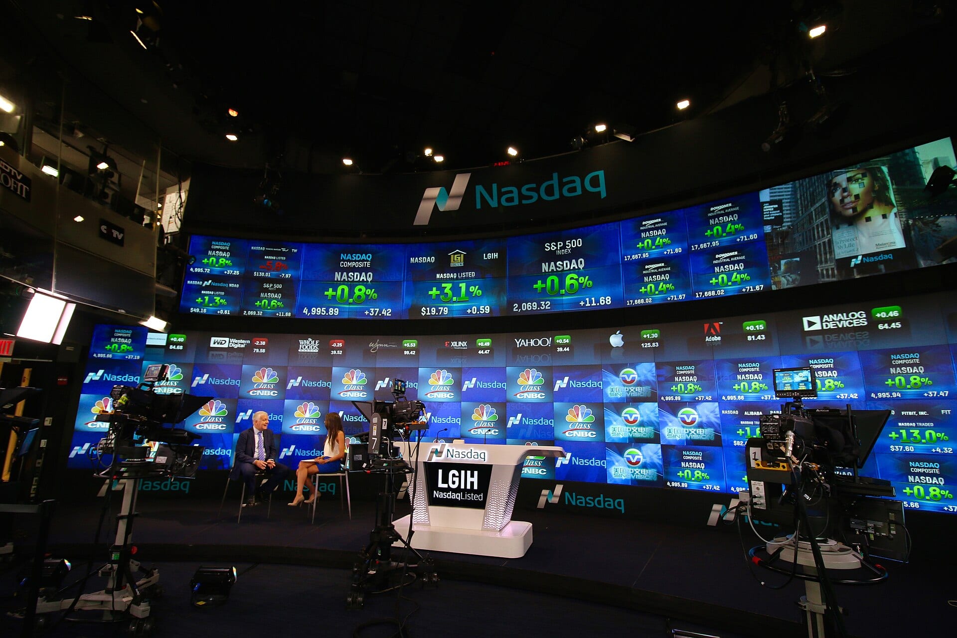 Estudio de televisión del Nasdaq con una pared curva de pantallas que muestran cotizaciones de índices y de empresas.