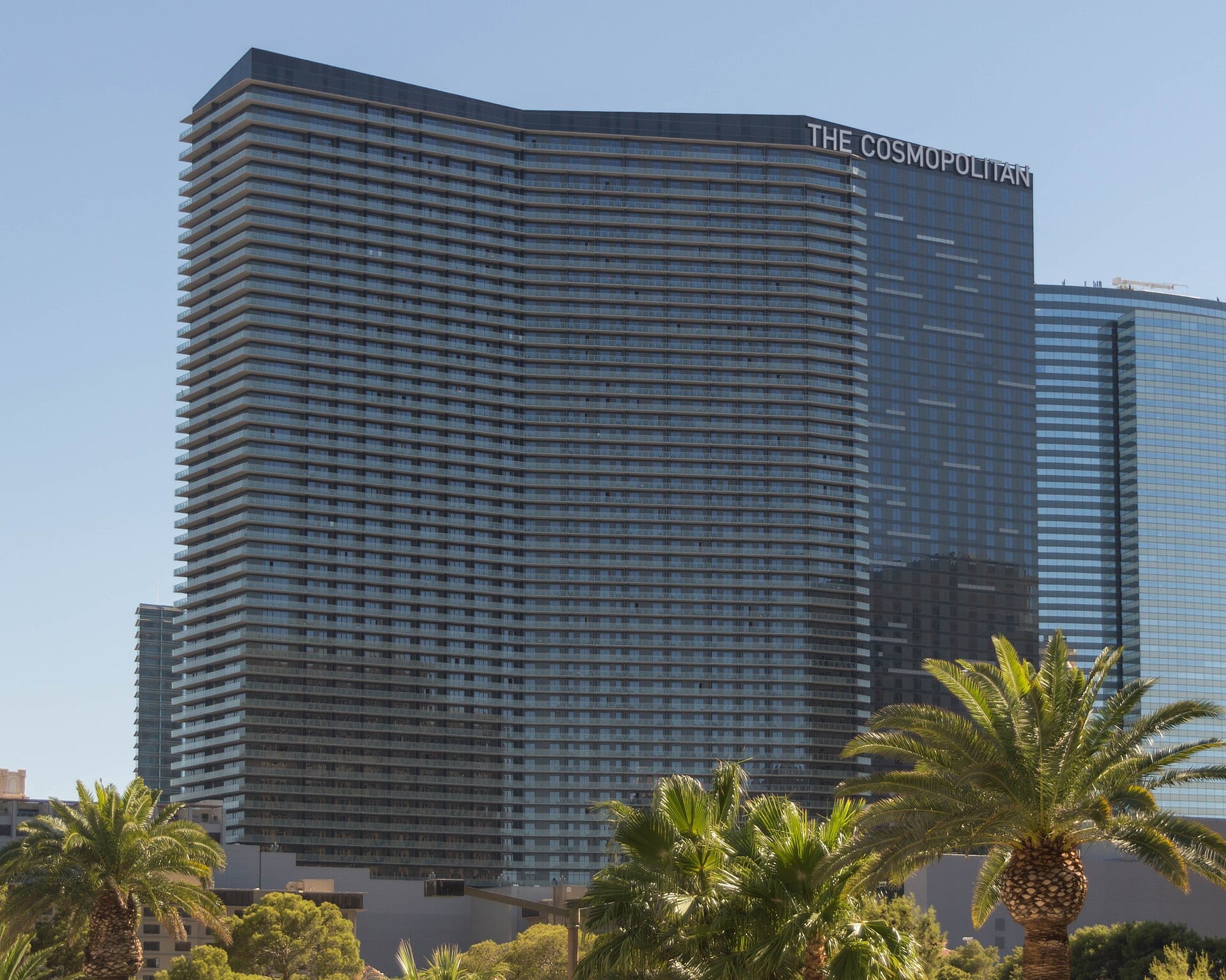 Torre de vidrio y balcones del hotel The Cosmopolitan, en Las Vegas, con palmeras en primer plano.