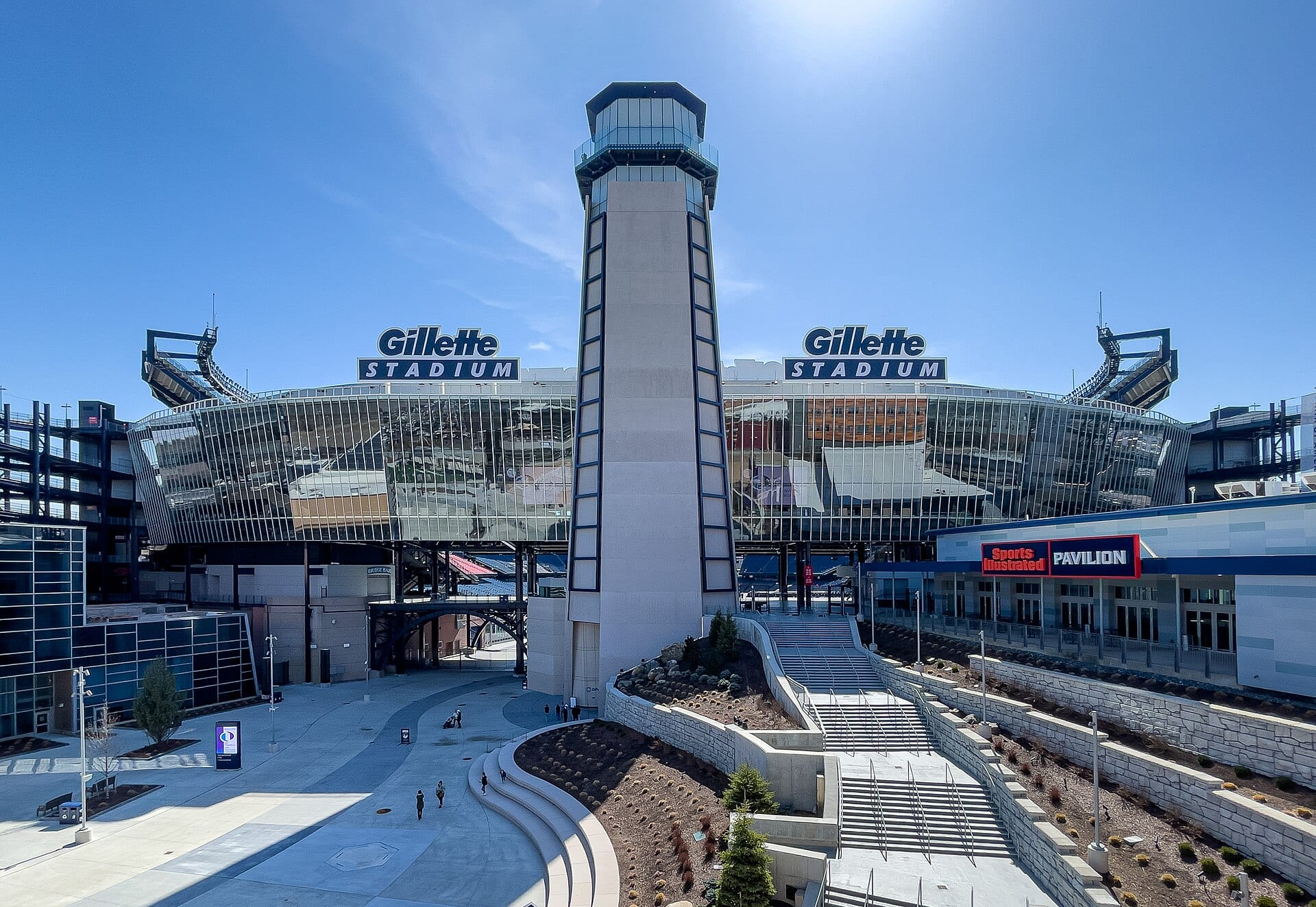 The glass facade of Gillette Stadium with its central tower and the stadium sign, under a clear sky.