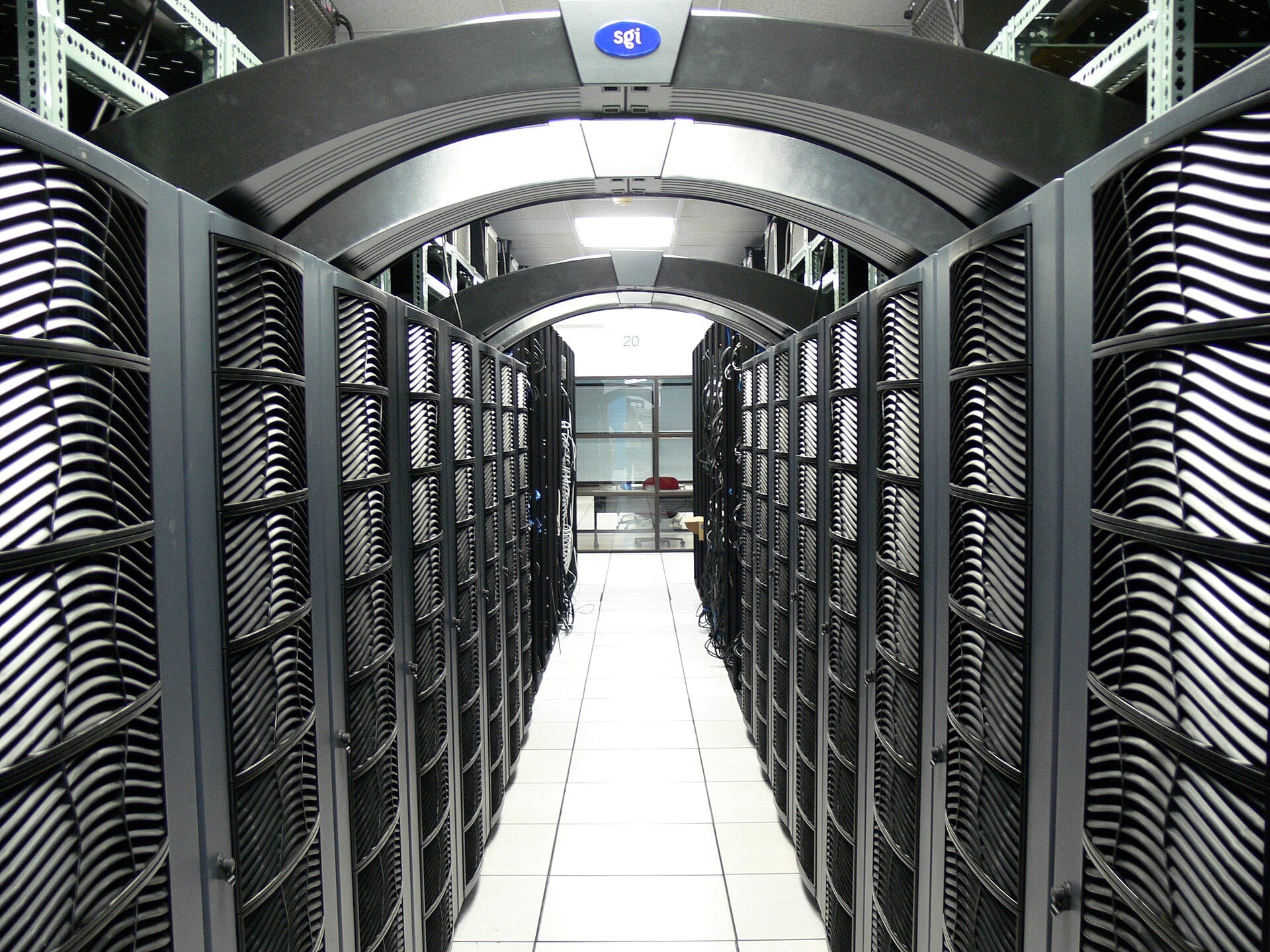 An aisle in a data center with black server cabinets on both sides and a metal arch overhead.