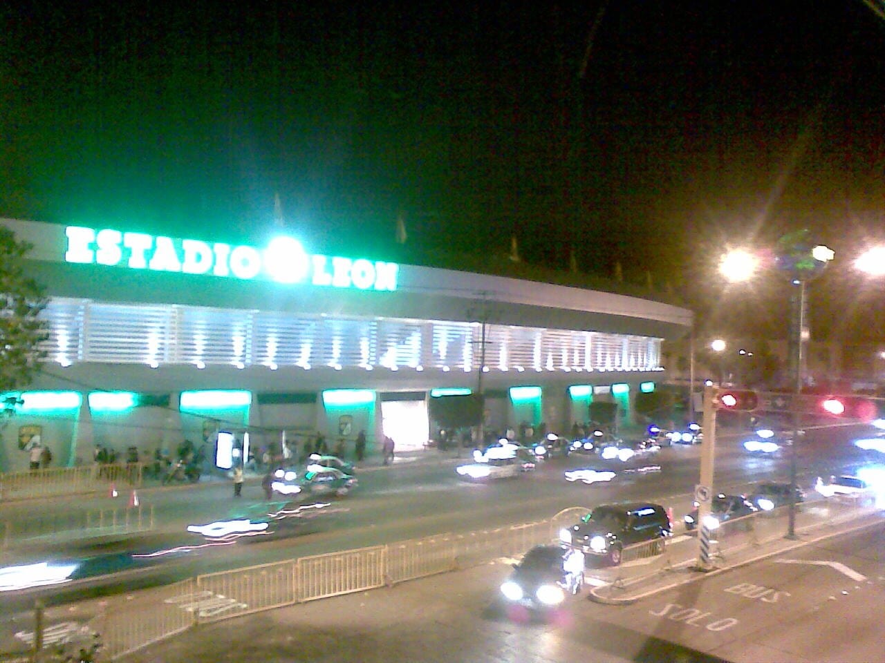 Fachada iluminada del Estadio León de noche, con tráfico y peatones frente a la entrada principal.