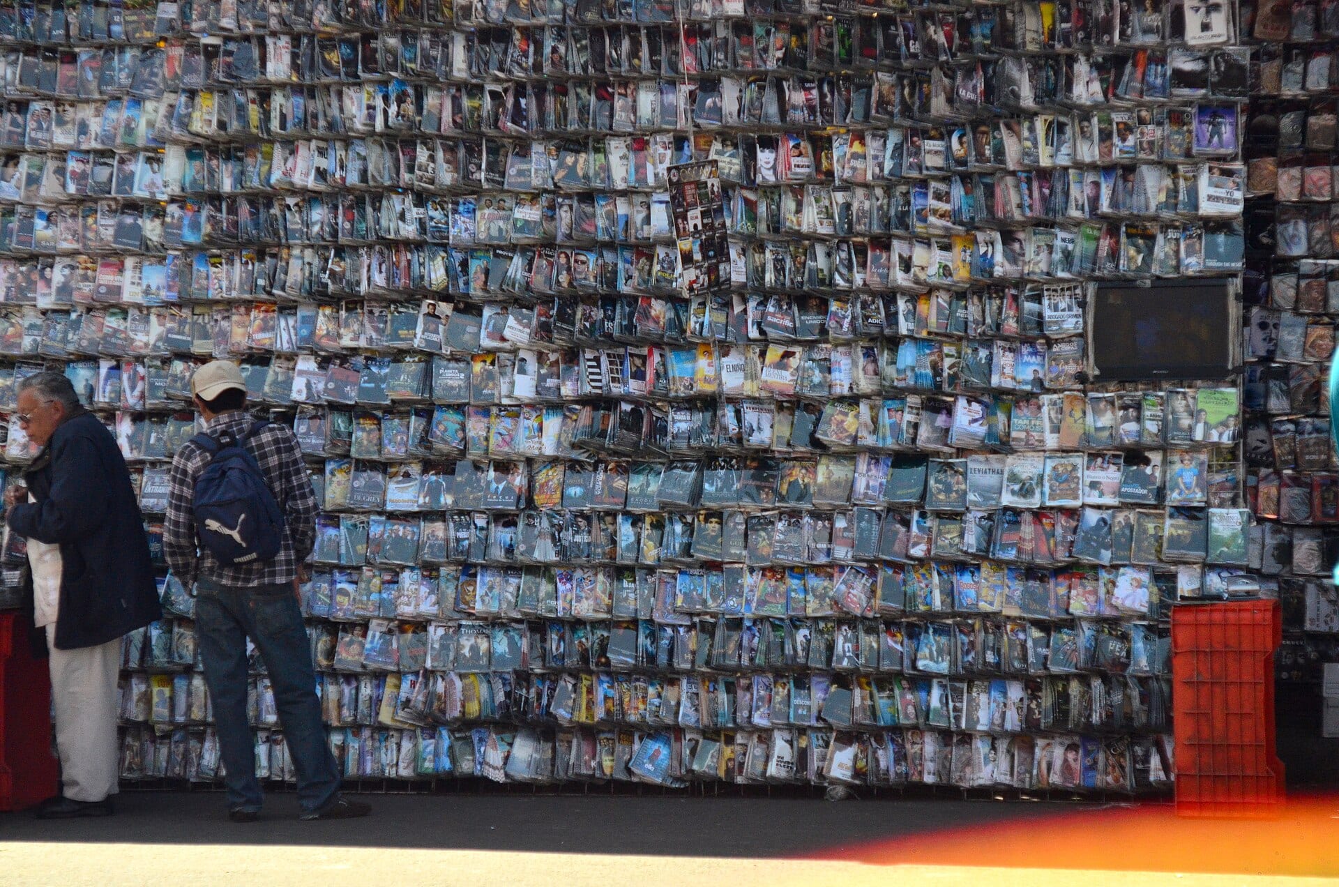 Una pared cubierta de discos en fundas de plástico en un puesto callejero de Tepito, con dos hombres de espaldas frente a ella.