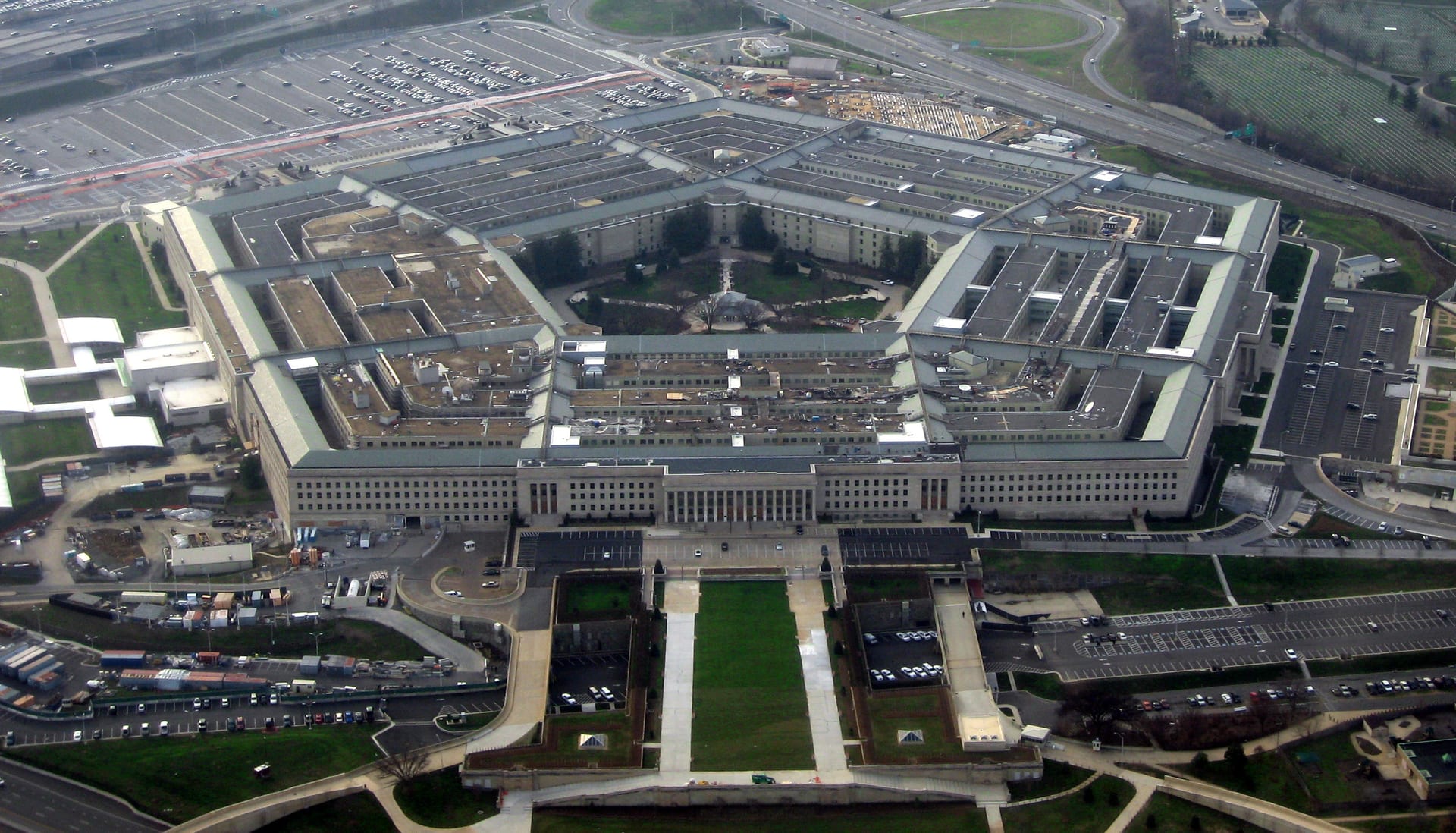 Vista aérea del edificio del Pentágono, de cinco lados, rodeado de estacionamientos y vías, con el río Potomac al fondo.