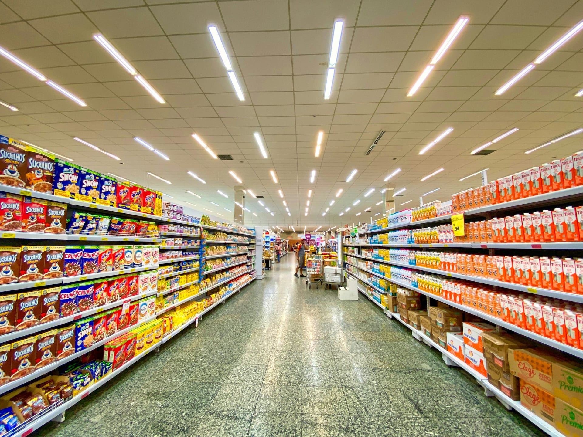 Pasillo de supermercado con estantes llenos de cajas de cereal a la izquierda y cartones de leche a la derecha.