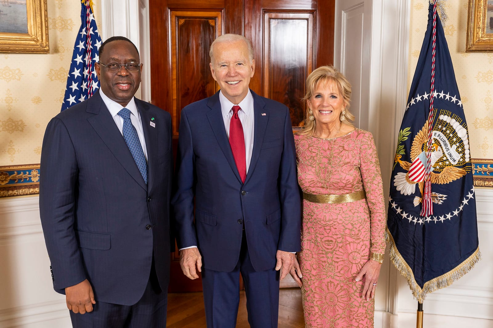 Macky Sall, in a dark suit, poses with Joe and Jill Biden in front of a U.S. flag and the presidential flag.