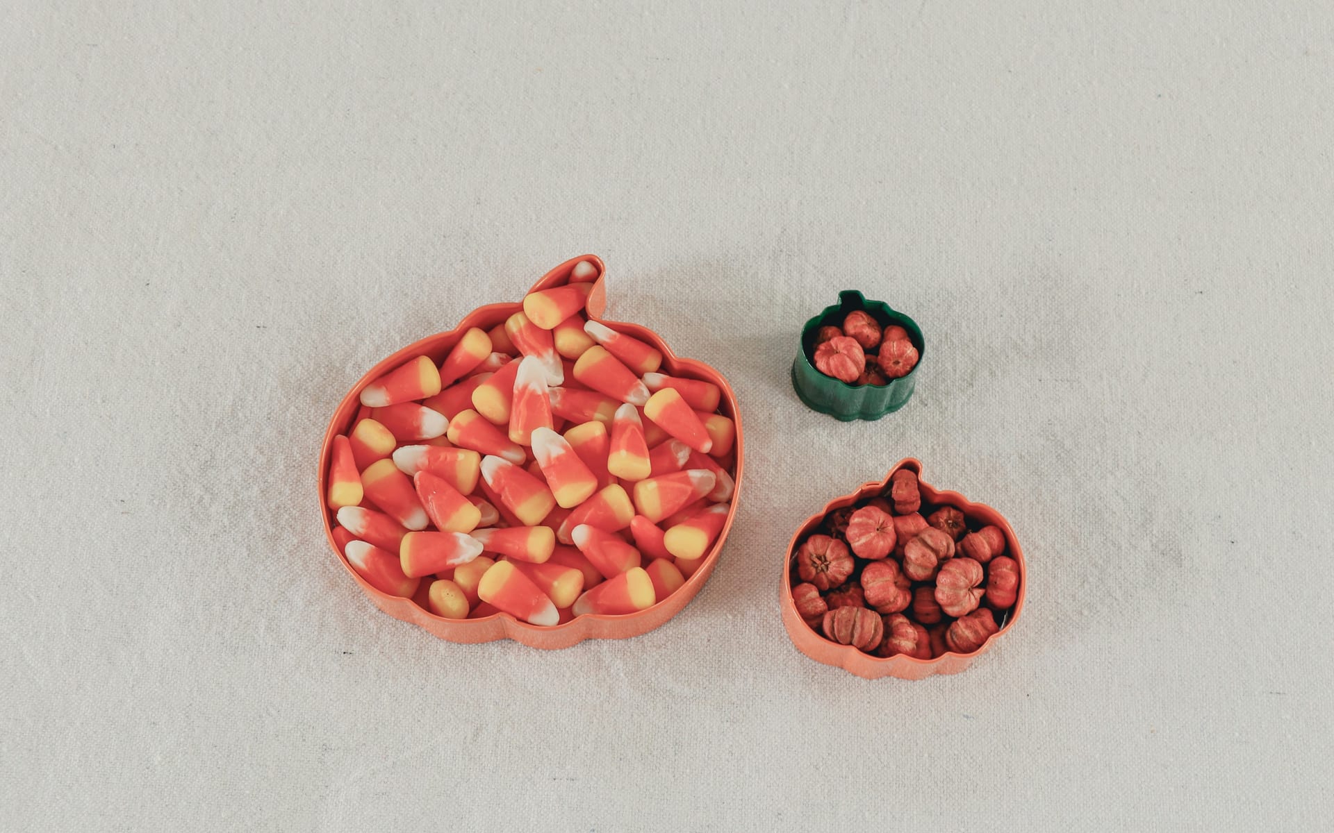 Una charola con forma de calabaza llena de dulces de maíz naranjas y amarillos, junto a dos moldes pequeños con calabazas diminutas, sobre un mantel claro.