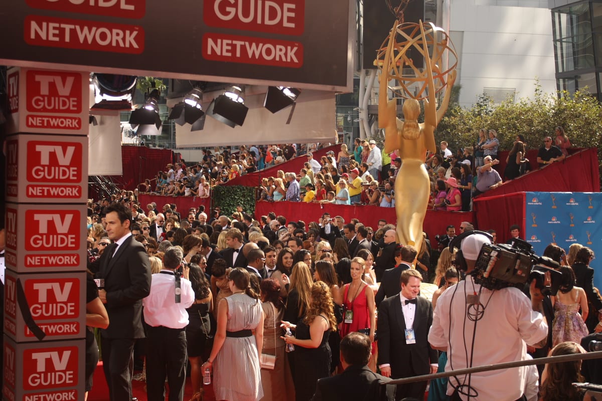 Una estatua dorada gigante de la figura alada del Emmy se alza sobre una alfombra roja llena de invitados, fotógrafos y un camarógrafo.