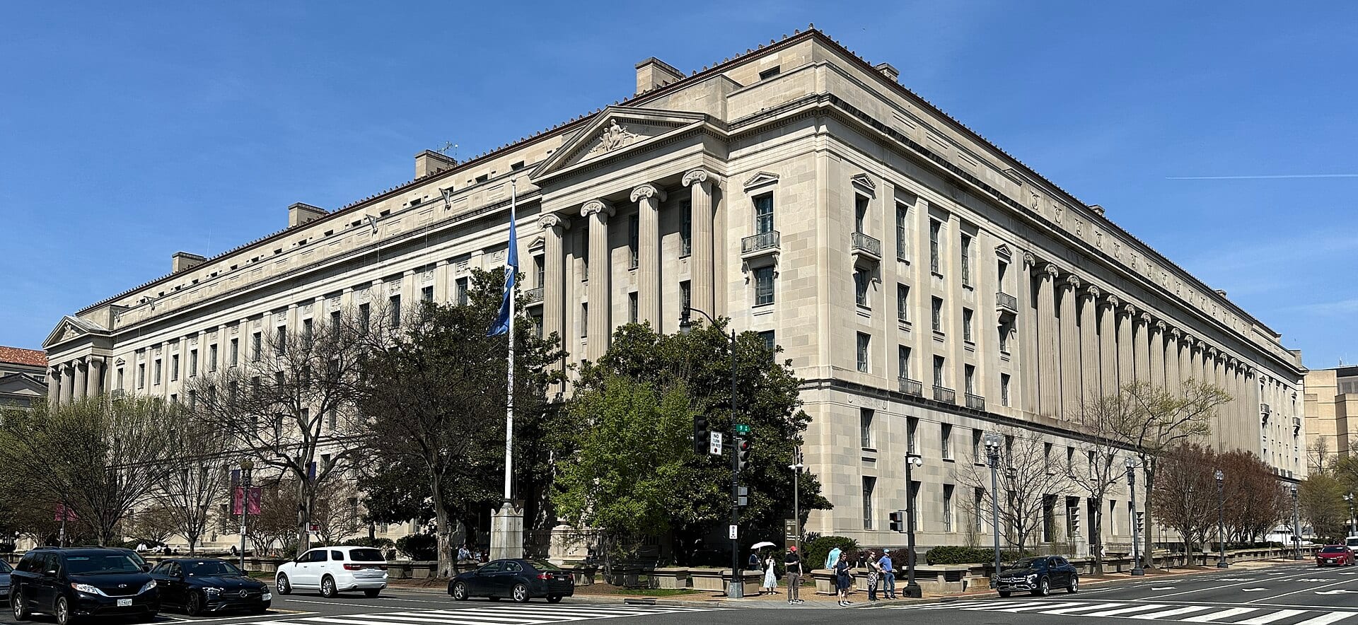The pale stone, colonnaded Robert F. Kennedy Department of Justice Building in Washington under a clear blue sky.