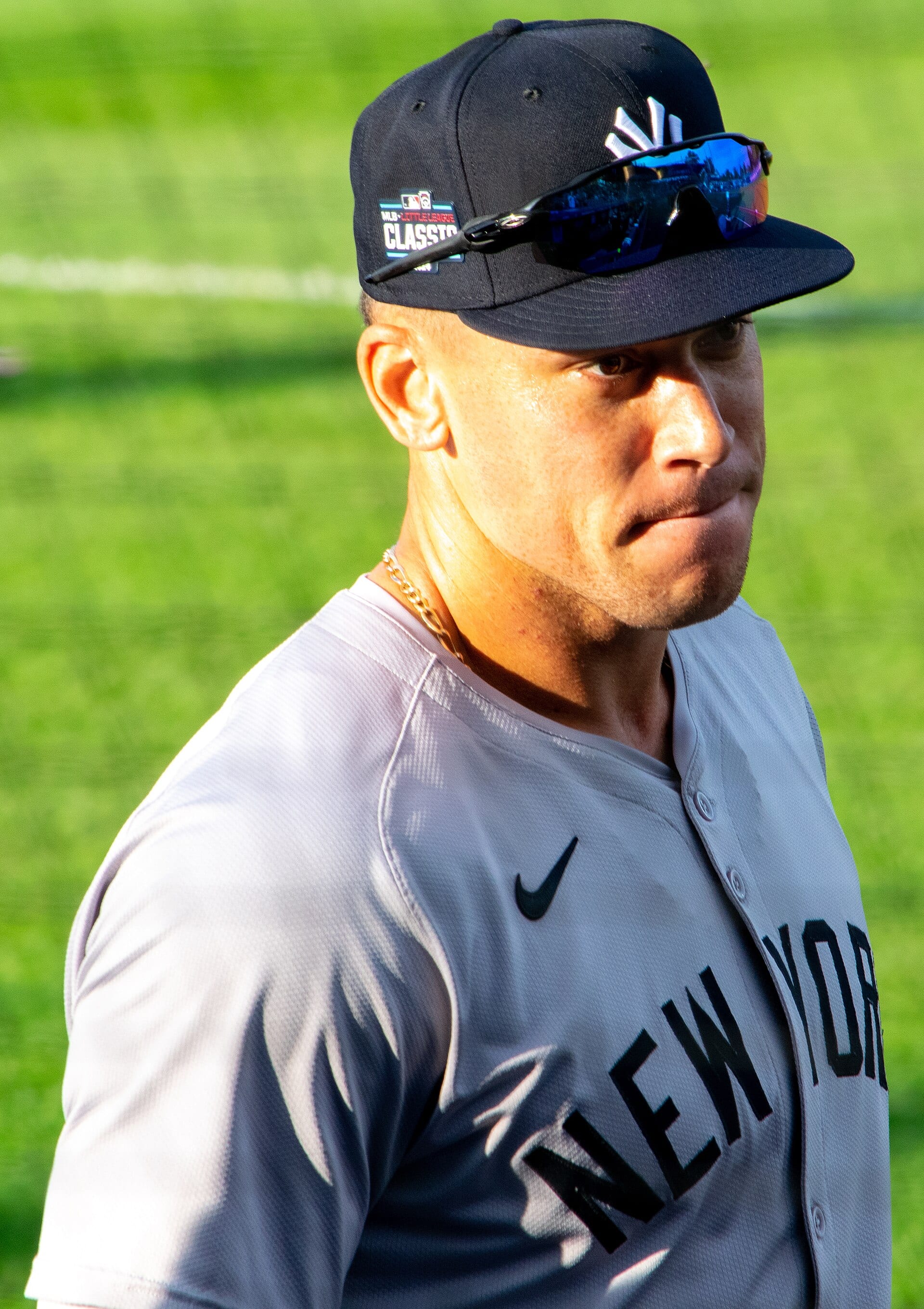 Aaron Judge, con gorra azul marino de los Yankees y lentes deportivos sobre la visera, mira hacia un lado sobre el césped en agosto de 2024.
