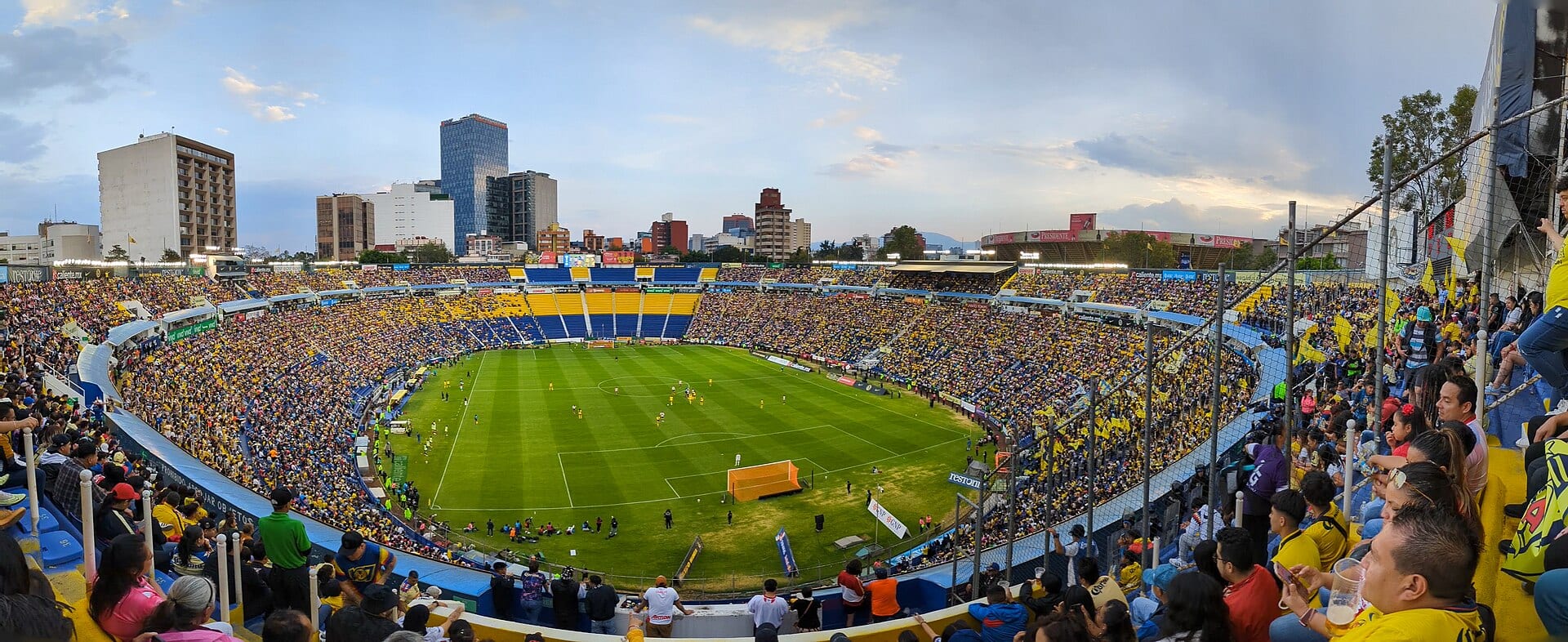 Vista panorámica del Estadio Ciudad de los Deportes lleno, con tribunas azules y amarillas y el campo de césped al centro.
