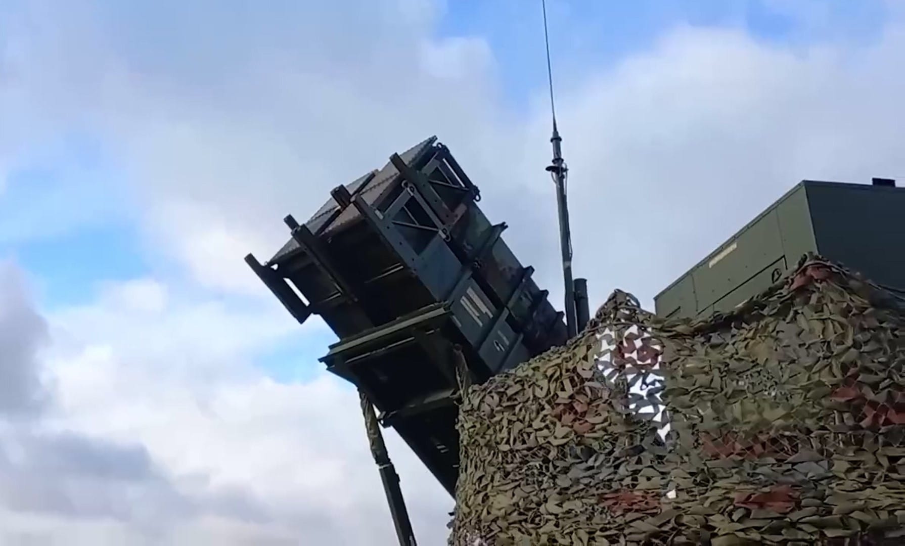 Contenedores de un lanzador de misiles Patriot inclinados hacia el cielo, parcialmente cubiertos por una red de camuflaje militar.