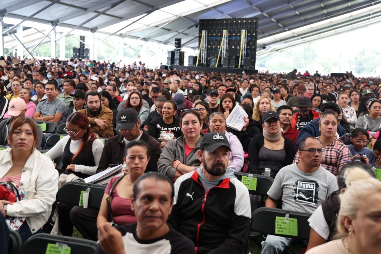 Cientos de personas sentadas bajo una carpa grande esperan el inicio de la entrega de vales del programa Mercomuna.