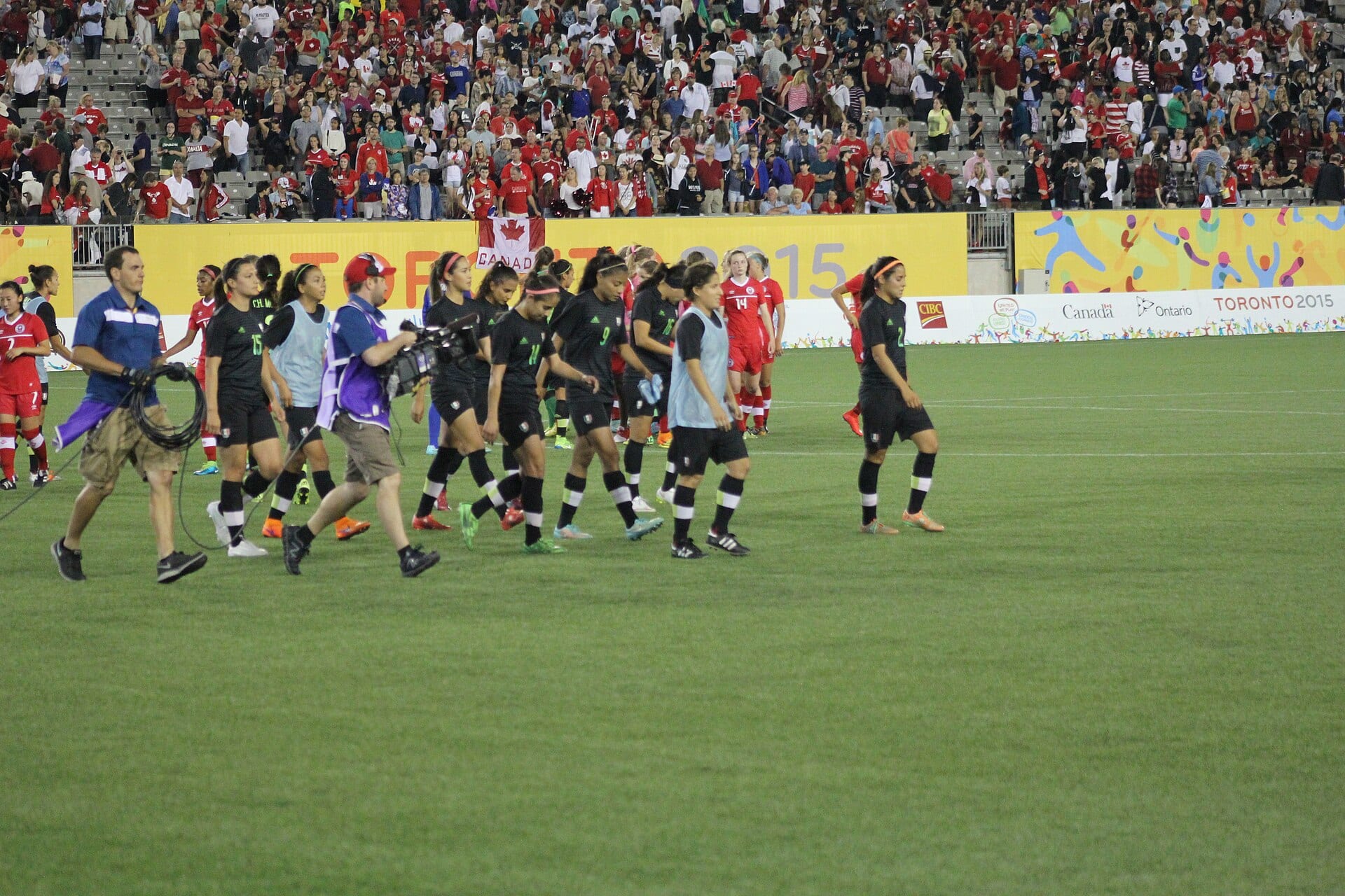 Futbolistas de la selección mexicana femenil con uniforme oscuro caminan por la cancha al final de un partido en Toronto 2015.