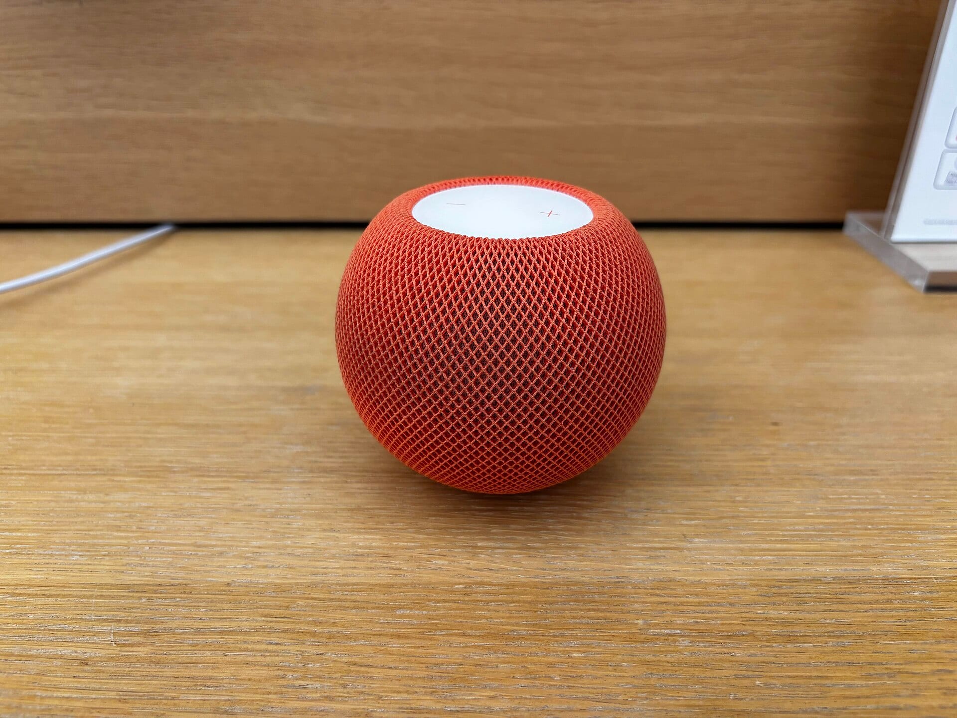 An orange HomePod mini, a spherical speaker with a fabric mesh, on a light wooden table.