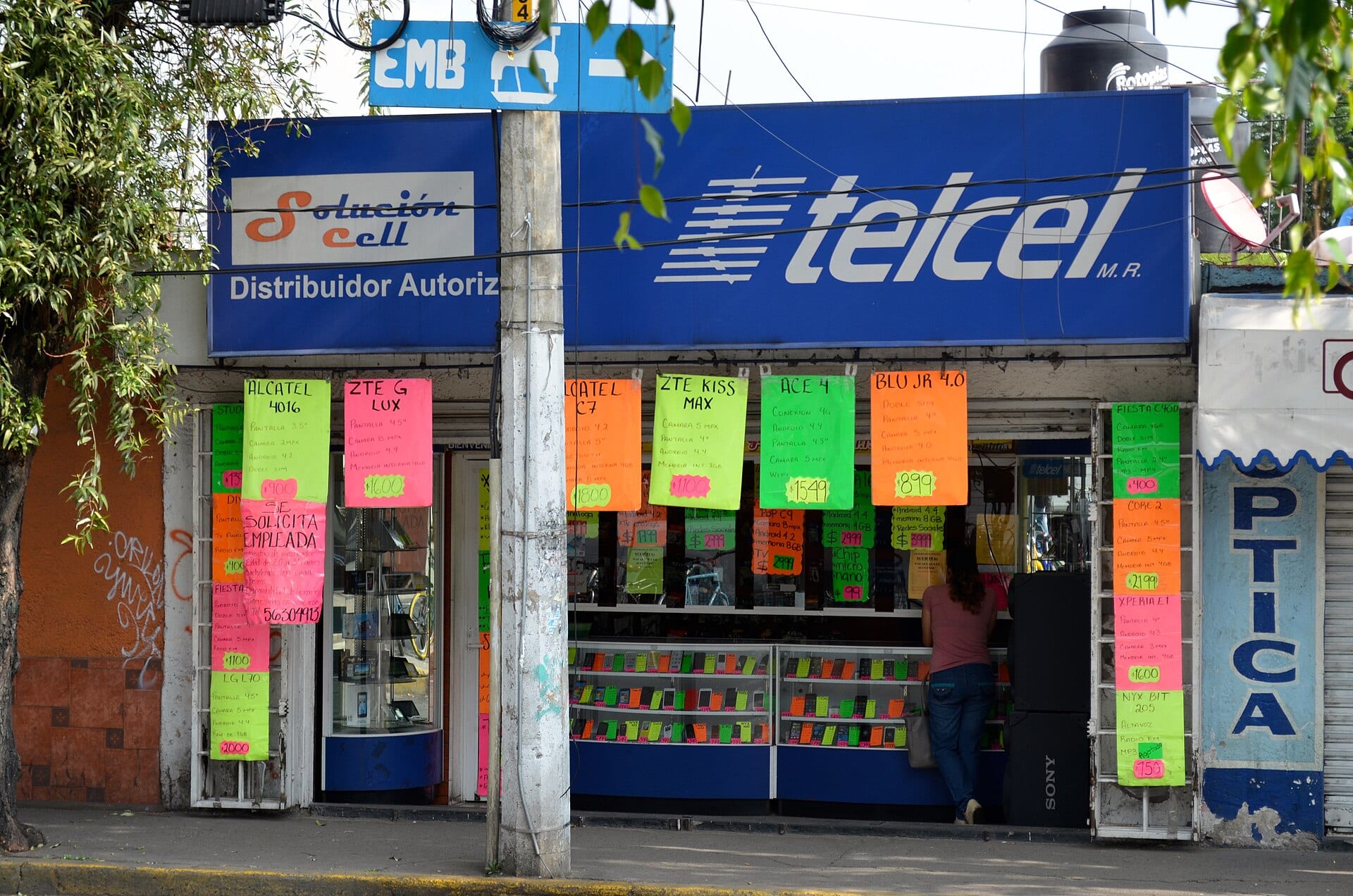Local de venta de celulares con un gran letrero azul de Telcel y hojas de colores con precios de teléfonos colgadas en la fachada.