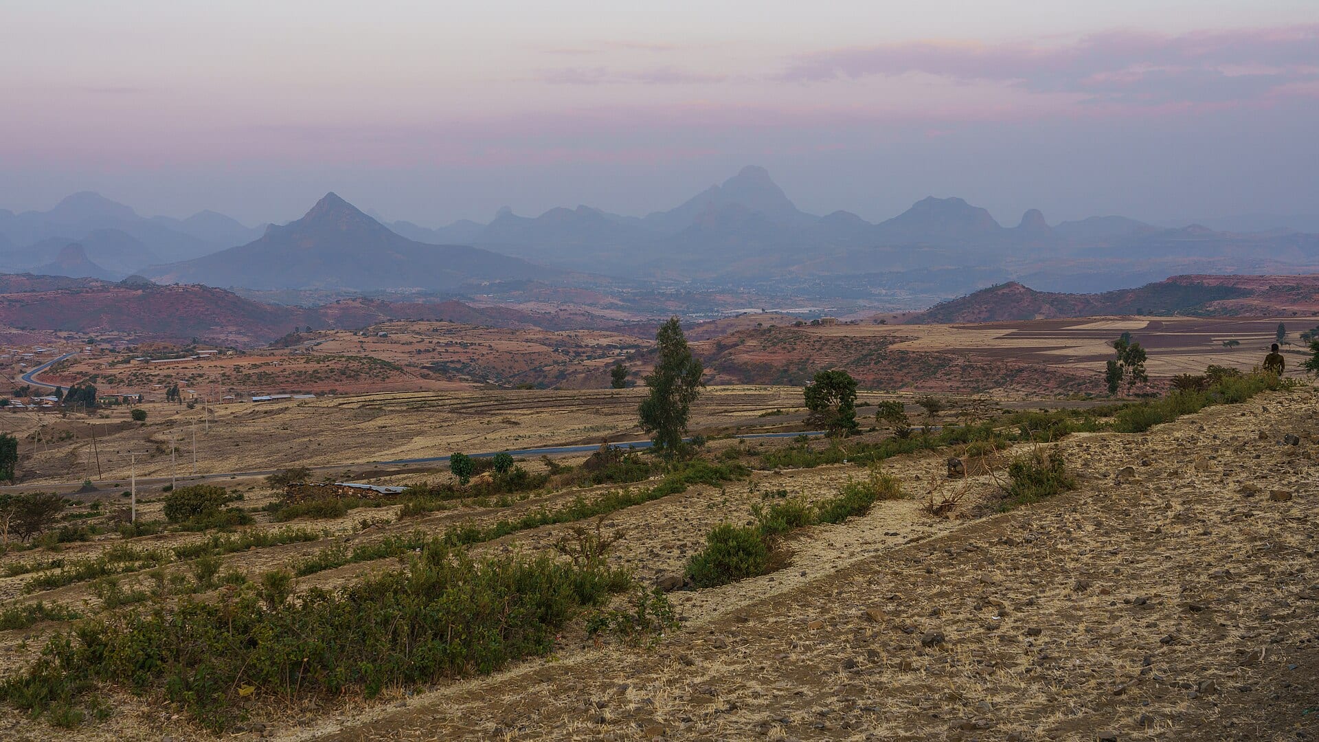 Colinas rocosas y campos secos en la zona de Adwa, en Tigray, con montañas al fondo bajo un cielo con nubes rosadas.