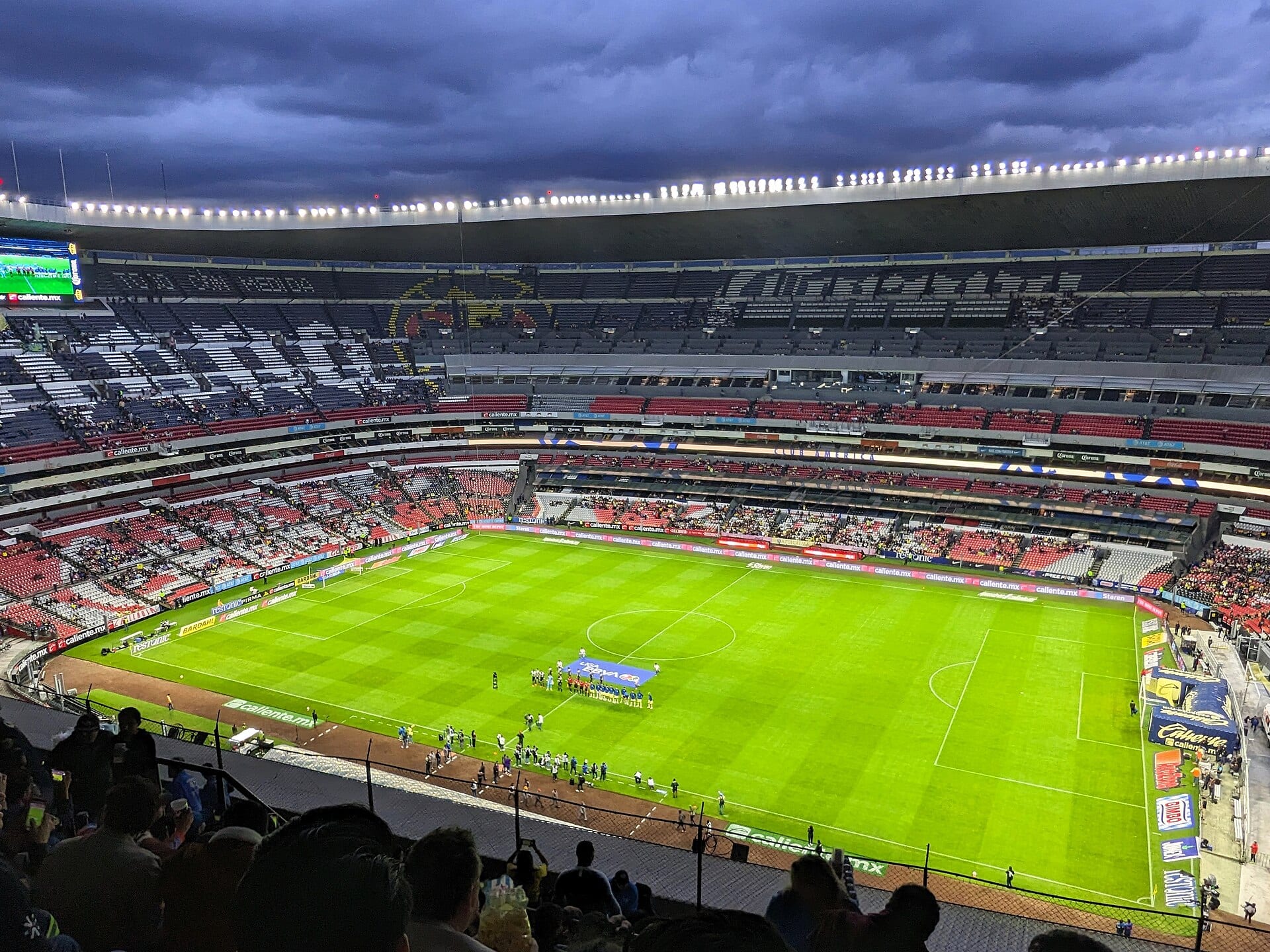 Jugadores de América y Necaxa disputan un balón sobre el pasto de un estadio con gradas llenas.