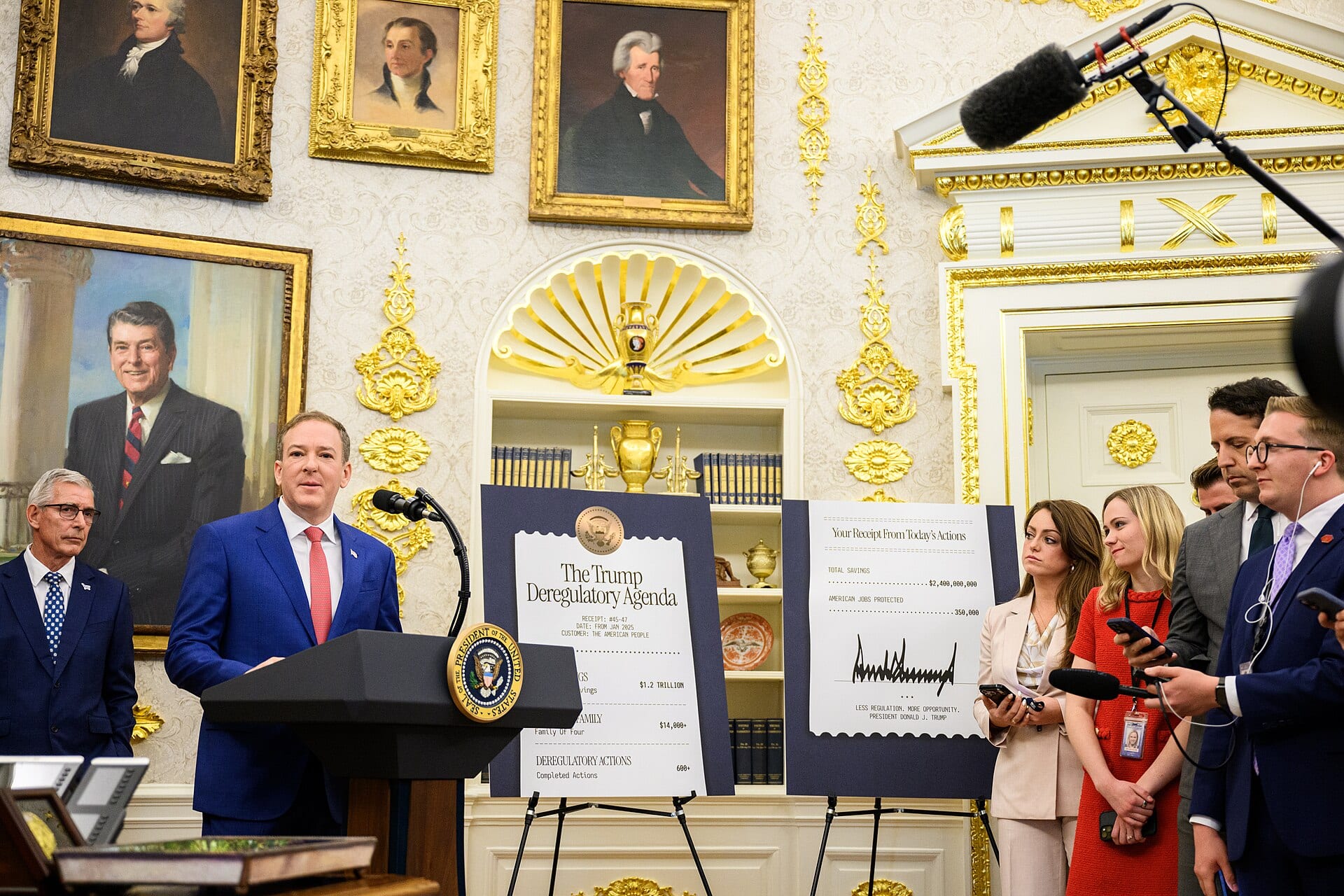 EPA Administrator Lee Zeldin speaks at a lectern bearing the presidential seal in the Oval Office, beside two easel boards and a group of reporters holding microphones.
