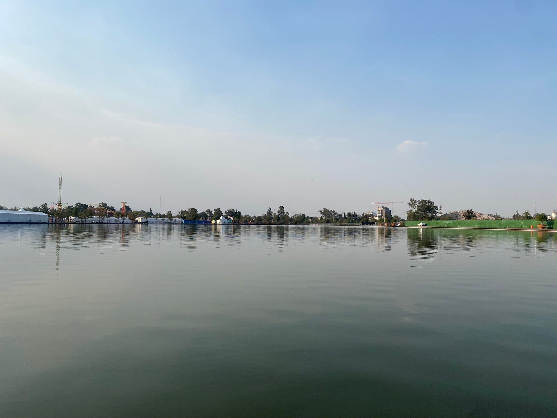 Vista del lago del Parque Bicentenario con el cielo despejado y, al fondo, carpas y juegos mecánicos a la orilla.