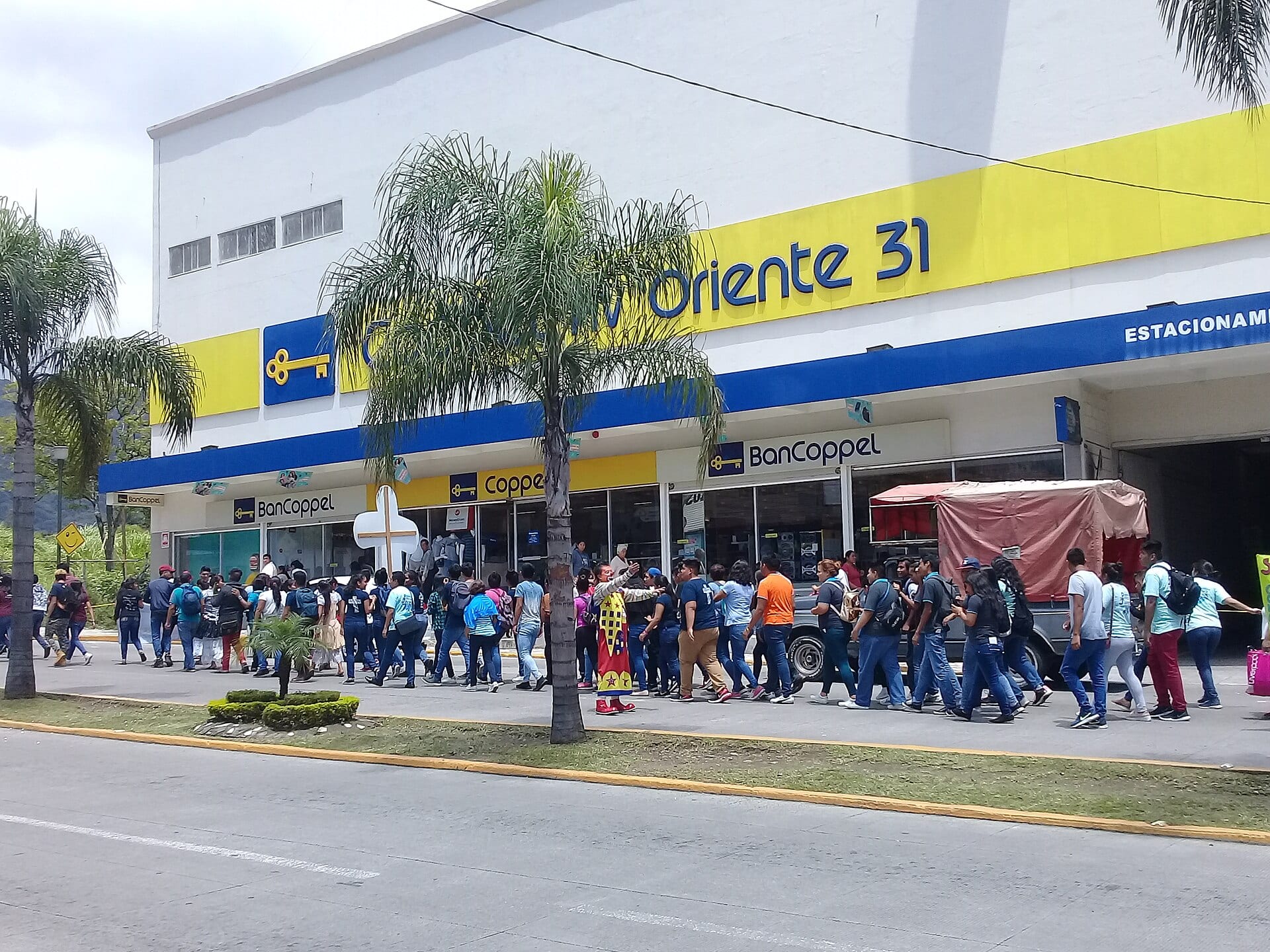 Fachada de una tienda Coppel con rótulos amarillos y azules y un grupo de personas que camina por la banqueta.
