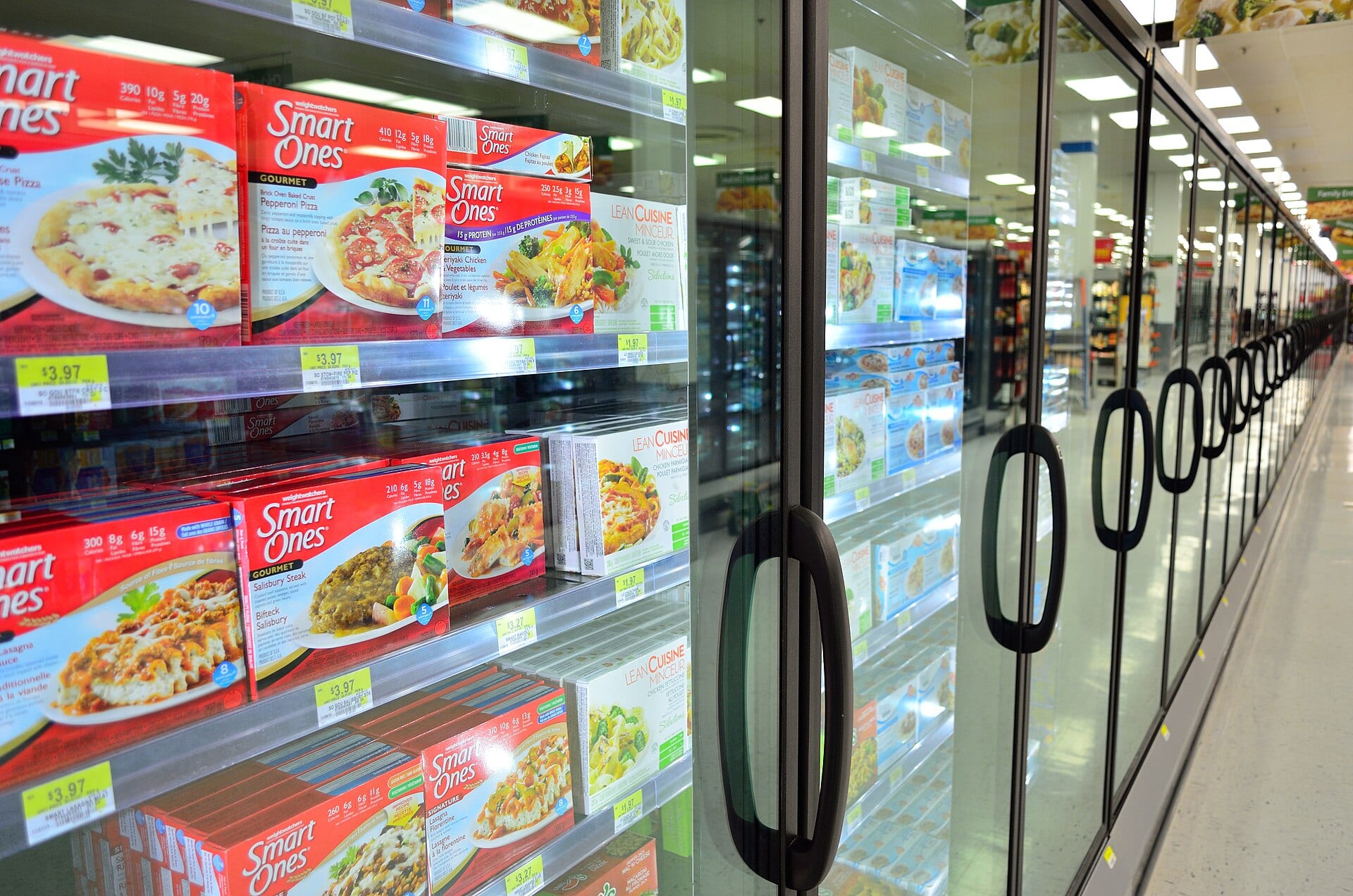 A supermarket aisle with glass doors showing boxes of frozen food on shelves.