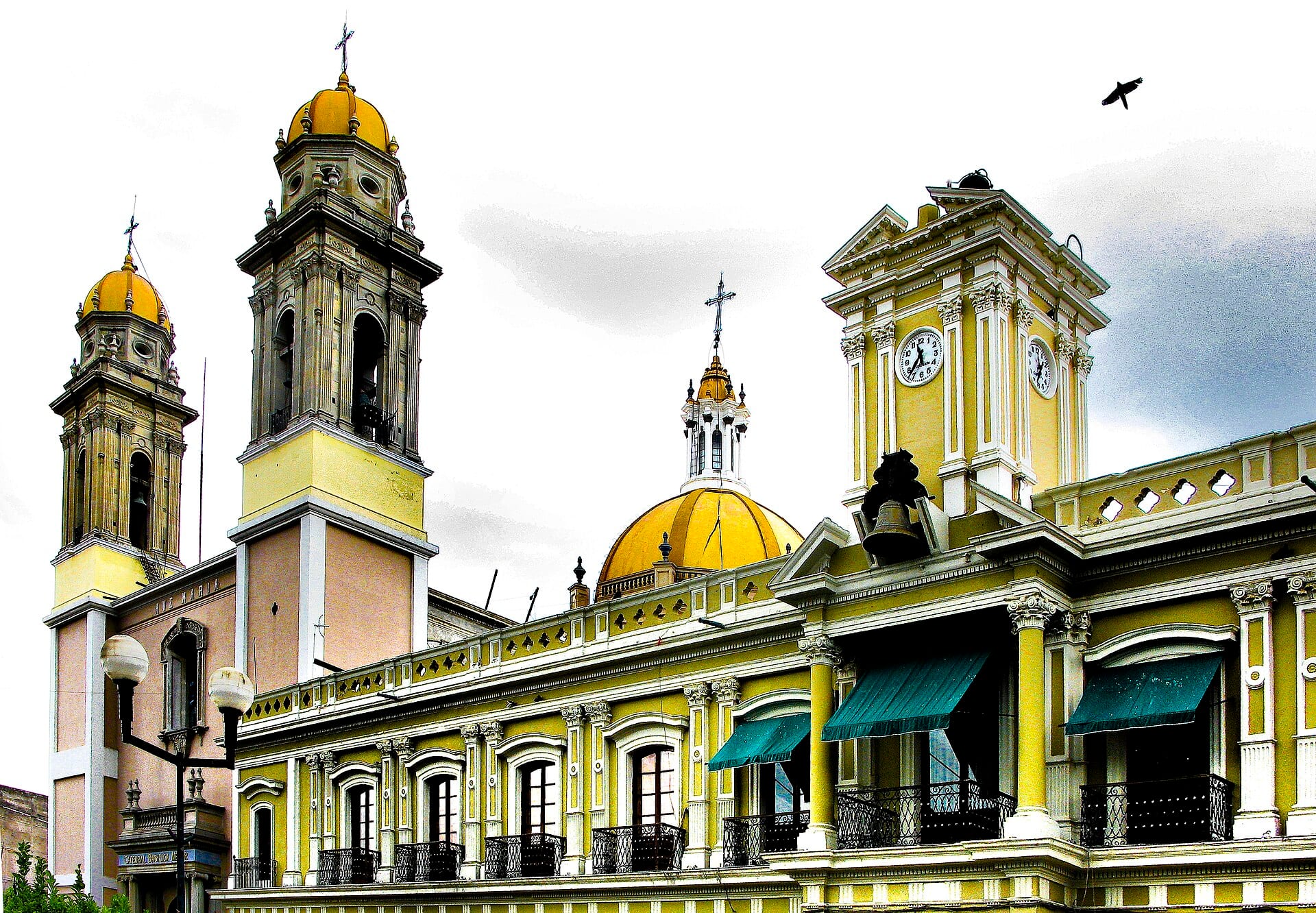 Torres amarillas de la catedral de Colima junto al edificio del Palacio de Gobierno, con su torre del reloj y balcones con toldos verdes.
