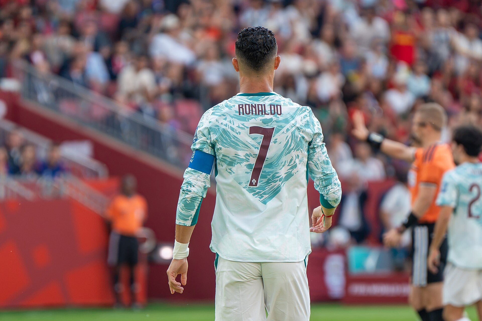 Cristiano Ronaldo, de espaldas, con el número 7 y el brazalete de capitán sobre el uniforme claro de Portugal, en un estadio lleno.