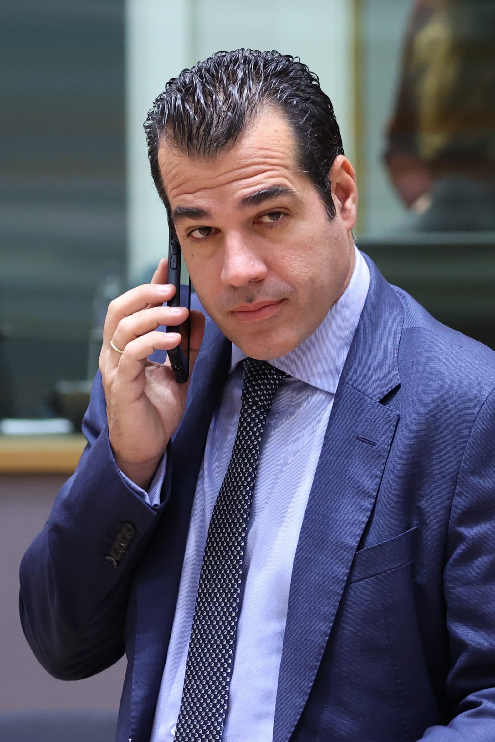 Un hombre de traje azul y corbata estampada habla por teléfono dentro de una sala de reuniones, con la mirada de lado.