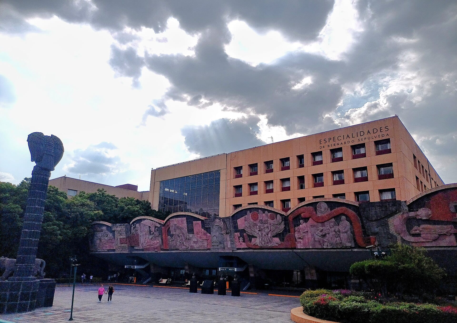 Edificio de Especialidades del Centro Médico Nacional Siglo XXI, con murales en relieve en la planta baja y una columna escultórica a la izquierda.