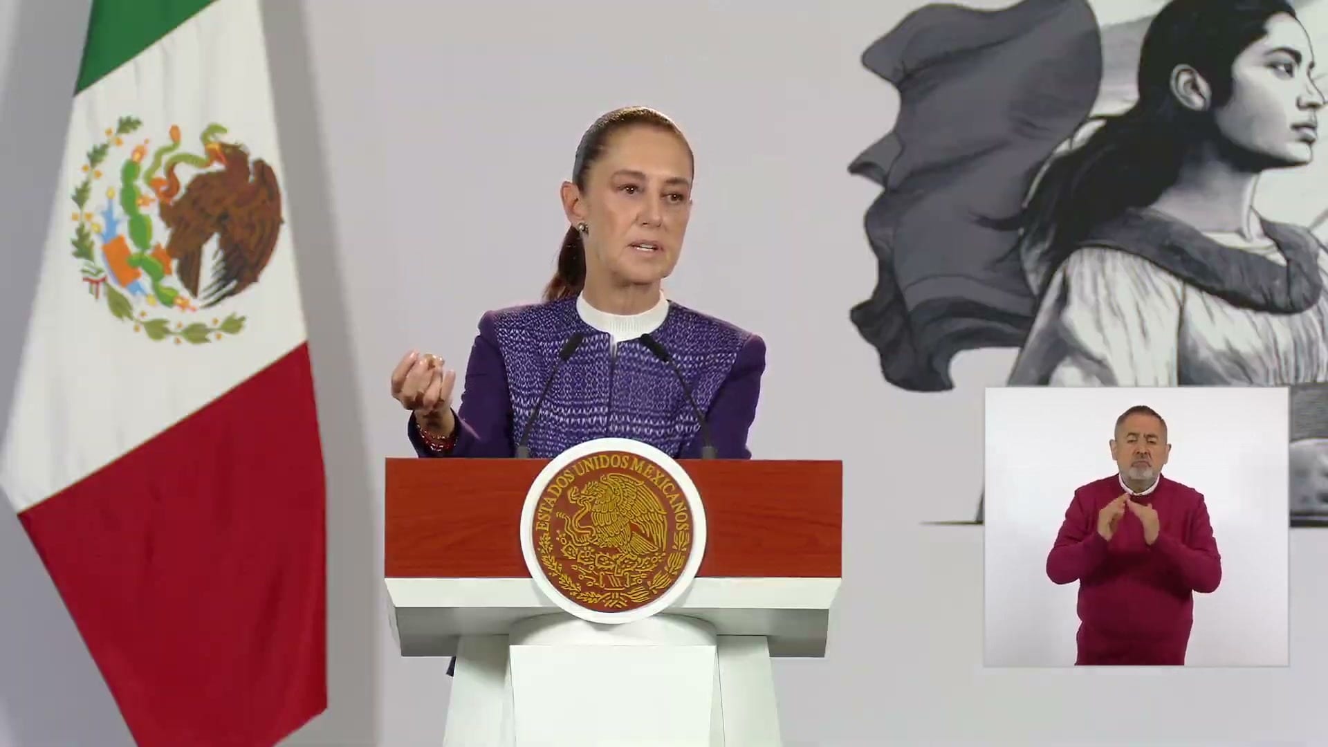 La presidenta Claudia Sheinbaum habla detrás de un podio con el escudo nacional, junto a una bandera de México.