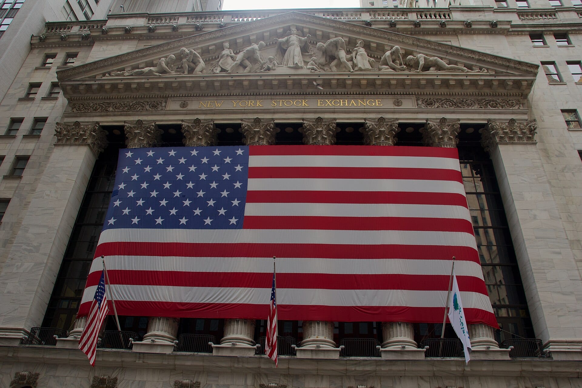 Fachada de mármol de la Bolsa de Nueva York, con su nombre en letras doradas y una bandera de Estados Unidos que cubre las columnas.
