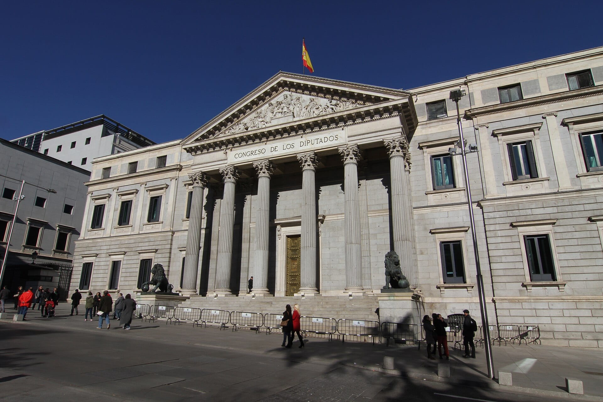The facade of Spain's Congress of Deputies in Madrid, with columns, two bronze lions and a Spanish flag above the pediment.