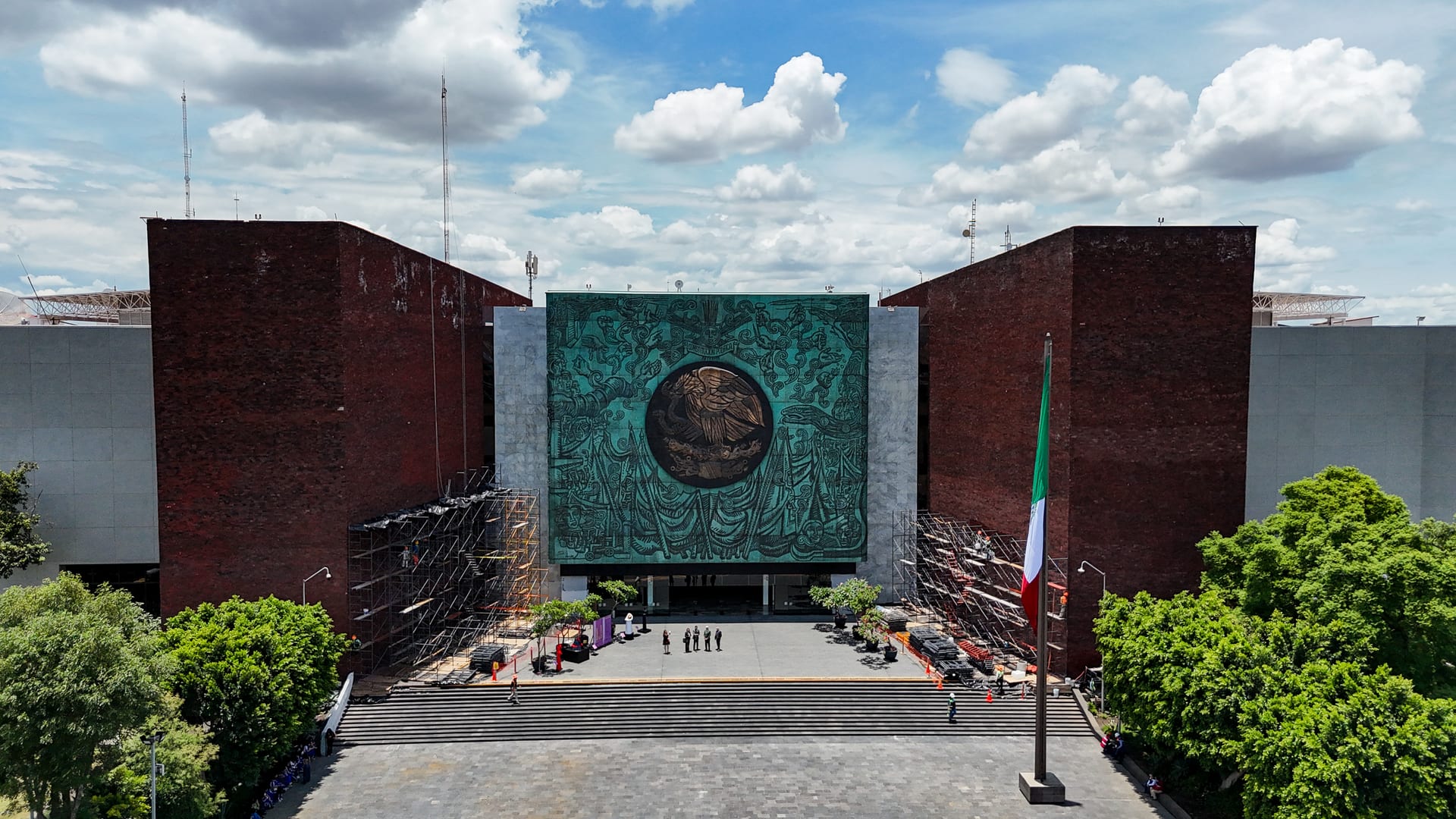 Vista aérea de la fachada del Palacio Legislativo de San Lázaro, con un mural del escudo nacional entre dos torres y andamios a los costados.