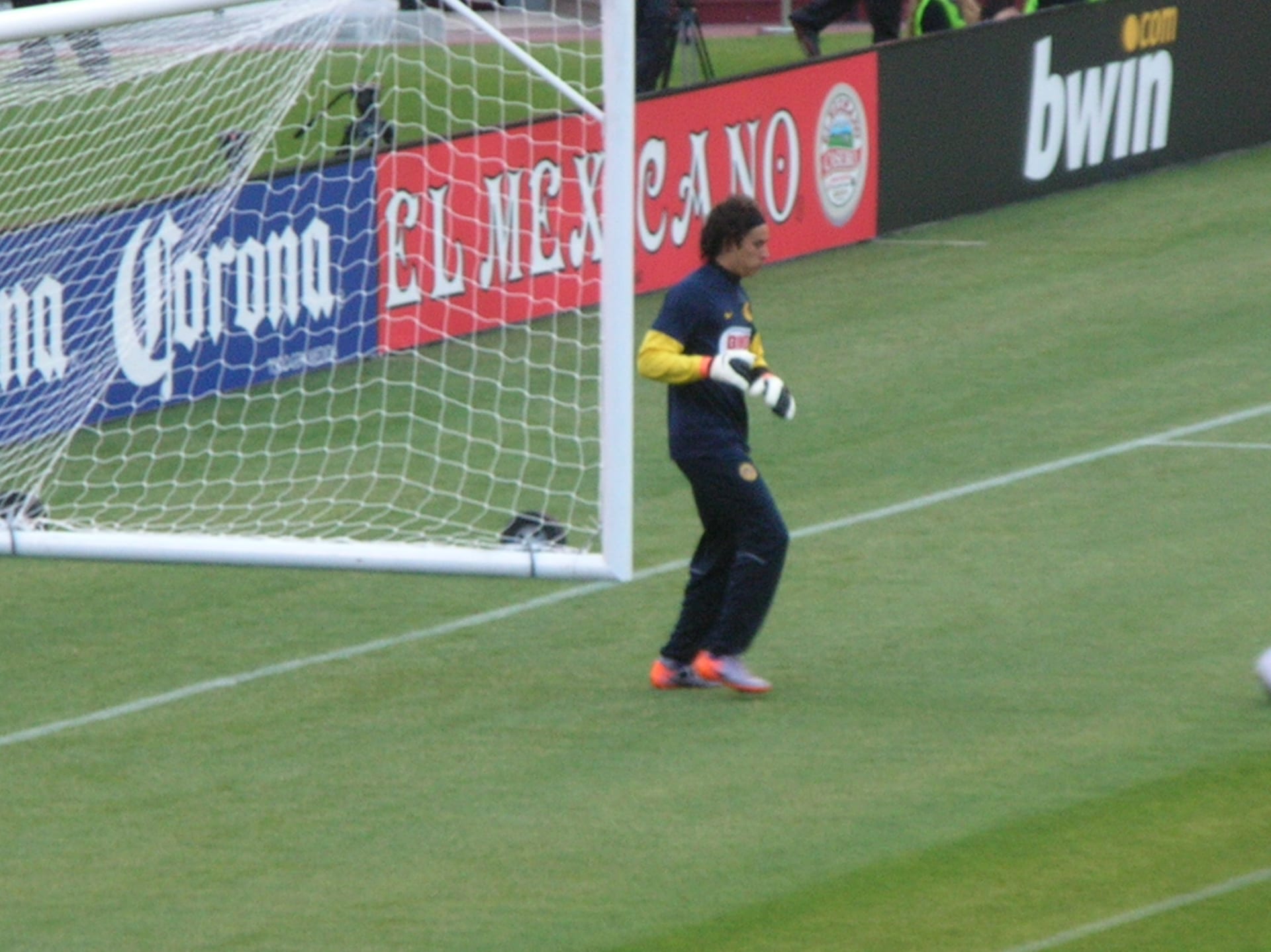 El portero Guillermo Ochoa, con ropa de calentamiento azul y amarilla del América, camina junto a una portería antes de un amistoso en 2010.