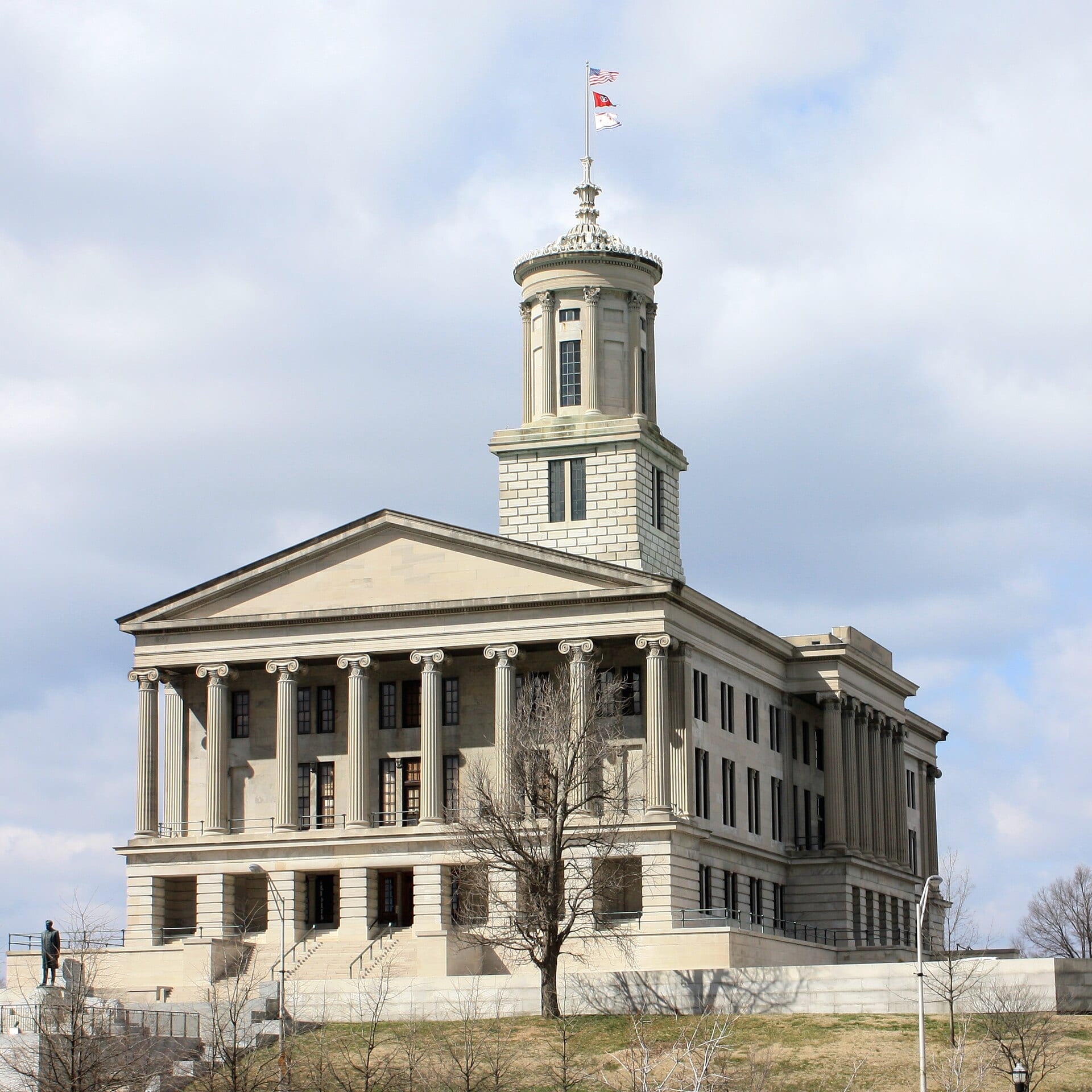 Fachada de piedra del Capitolio de Tennessee, con columnas y una torre central, bajo un cielo nublado.