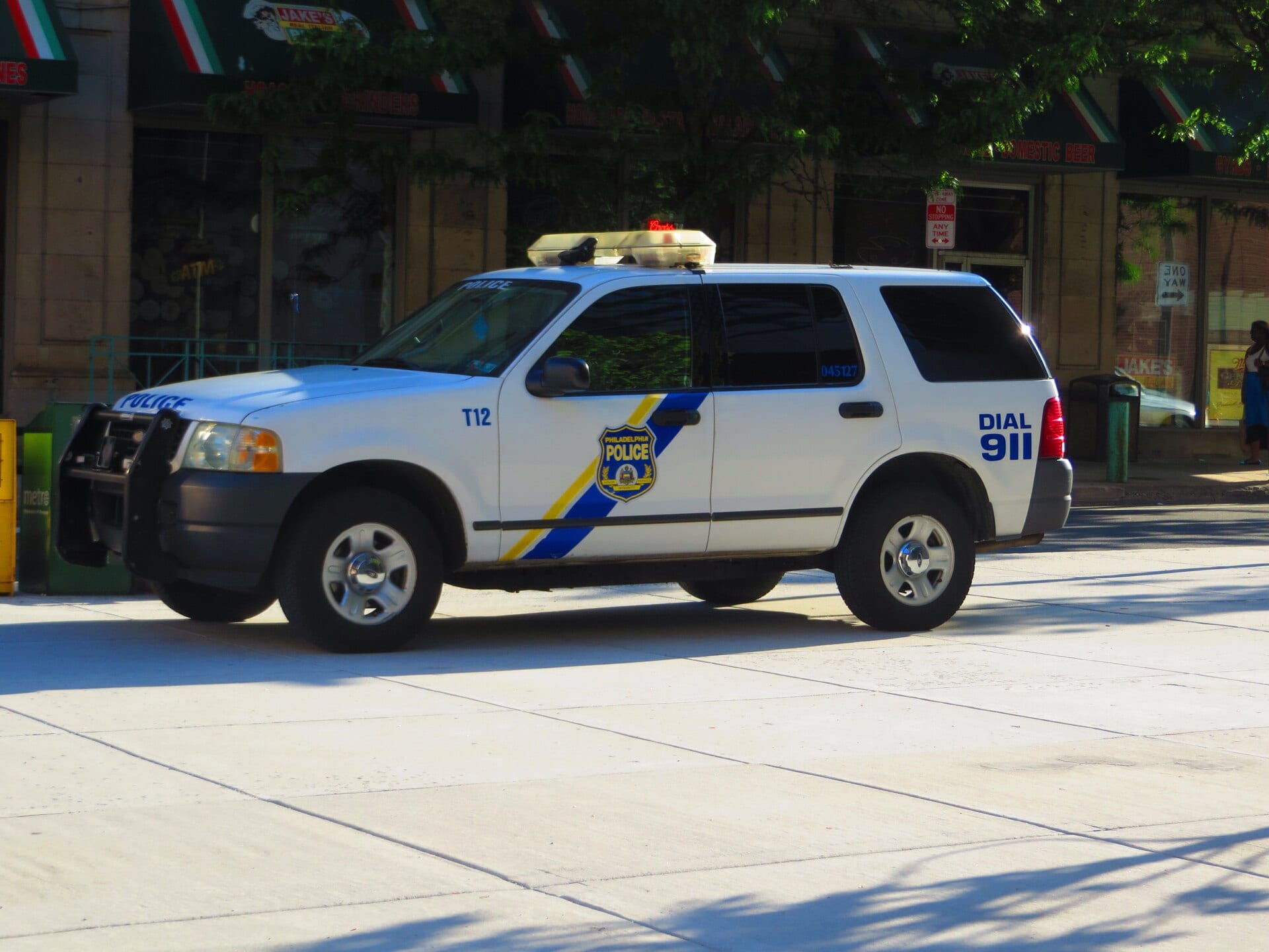A white Philadelphia police SUV with a blue and yellow stripe and the words Dial 911 parked on a downtown street.