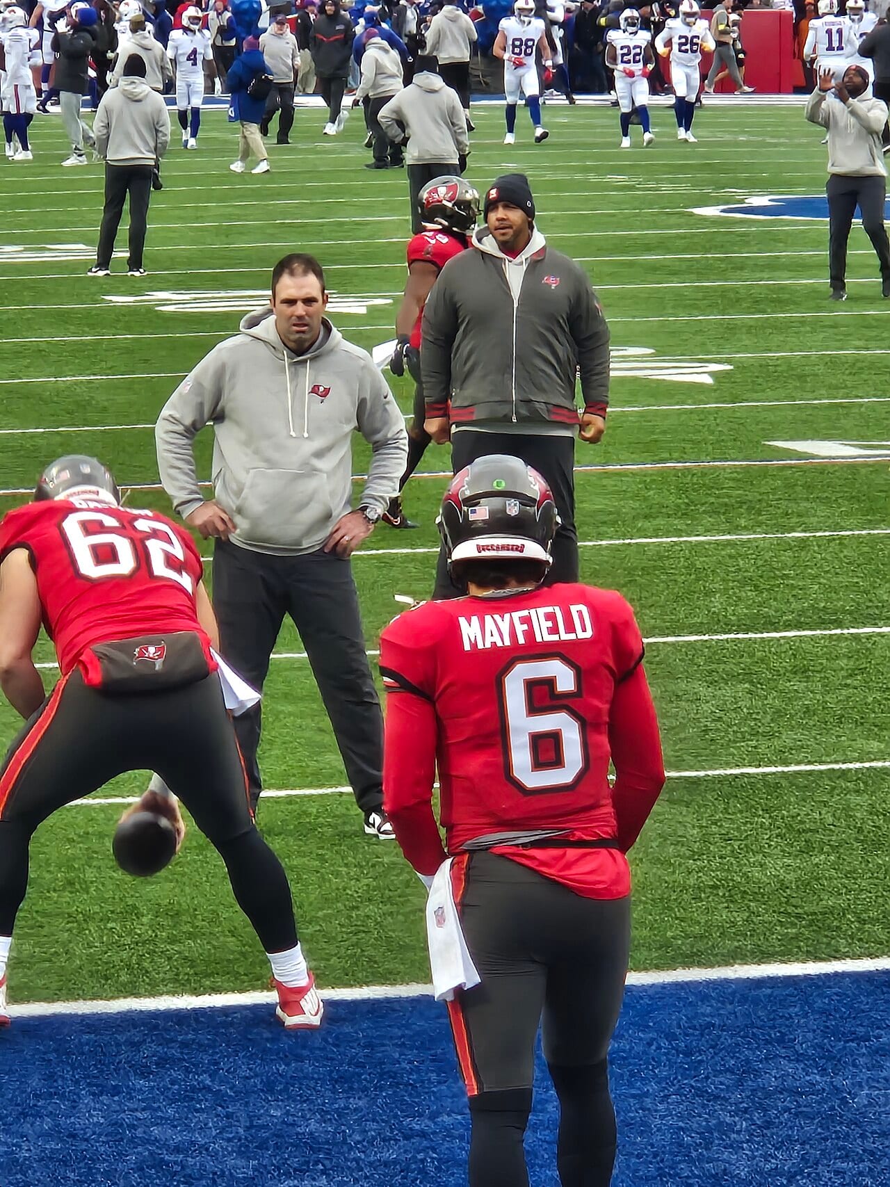 Baker Mayfield, de espaldas con el número 6 del uniforme rojo de Tampa Bay, calienta en el campo junto a un centro agachado.