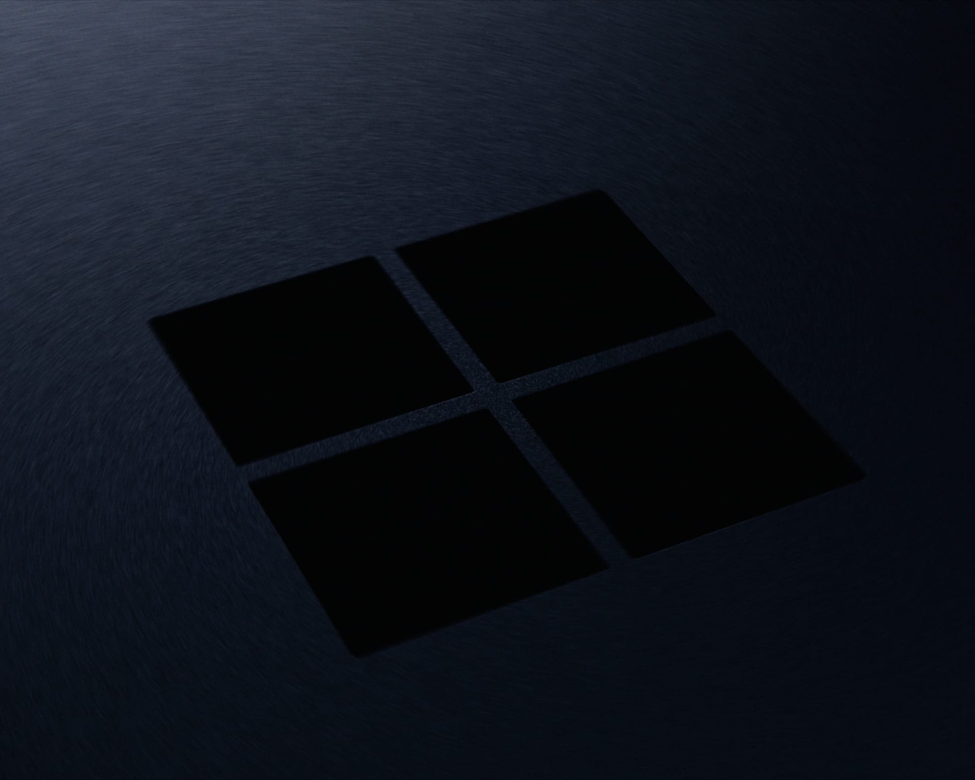Logotipo de Windows de cuatro cuadros en negro, grabado en una superficie metálica azul oscura de acabado cepillado, vista en ángulo.